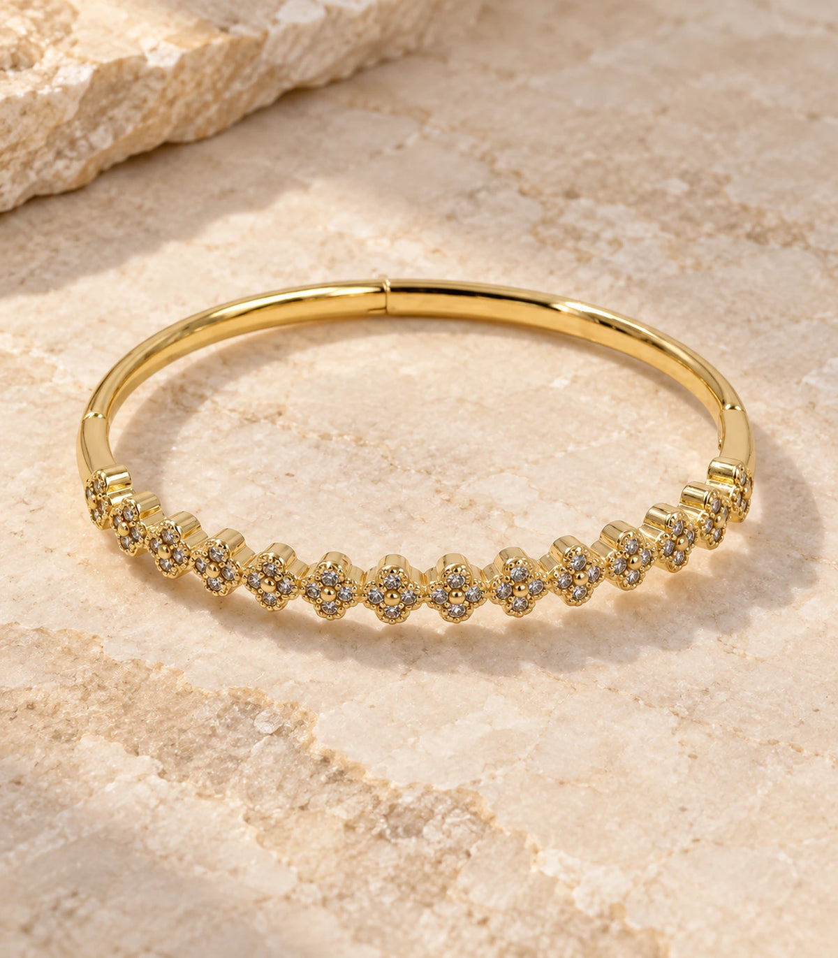 JIMIKI Gold-Tone Crystal Clover Row Bangle — bangle in a styled flat lay #color_gold-tone / clear