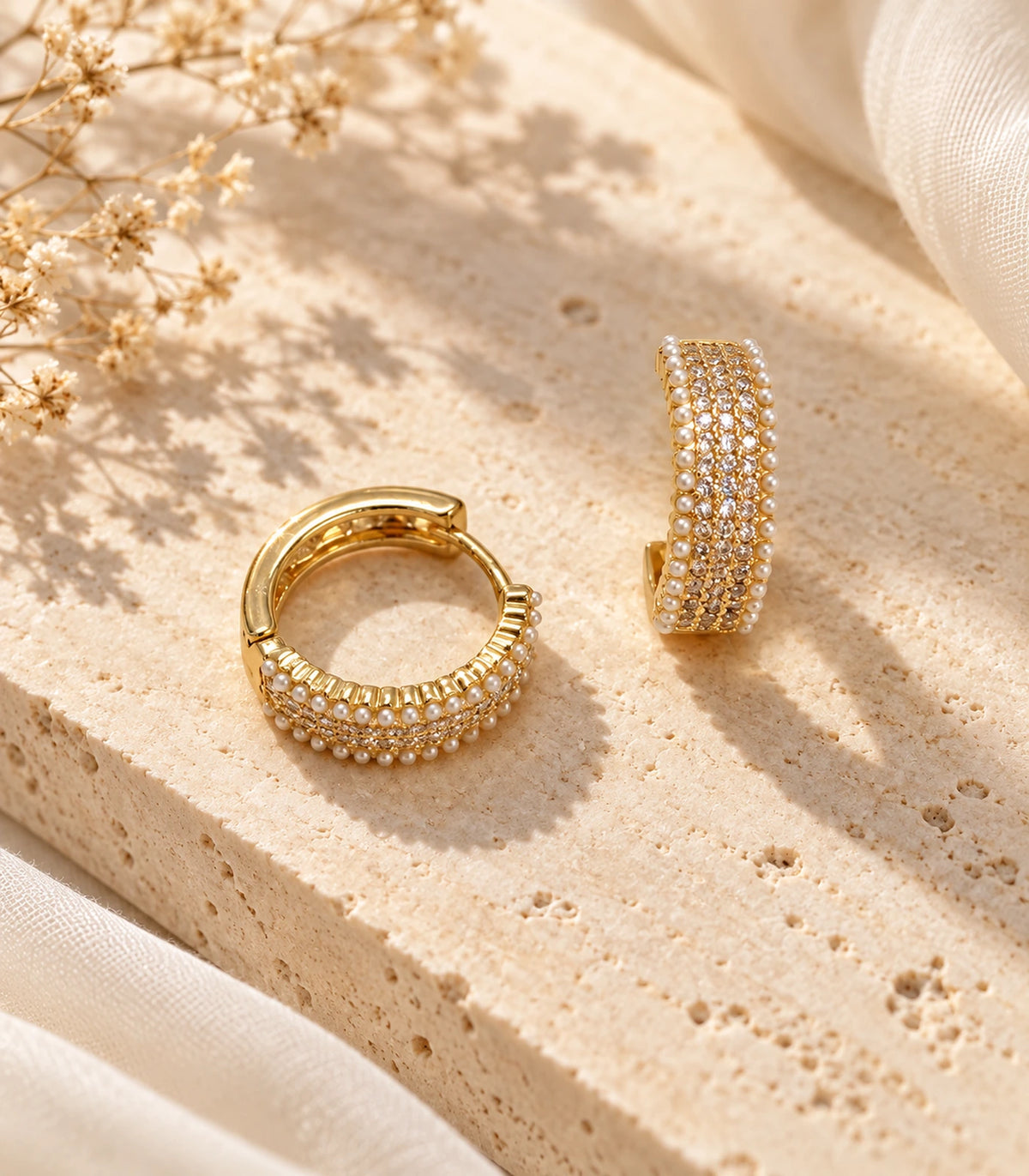 Pair of gold-tone crystal-style and white pearl-style border hoops on a warm stone surface