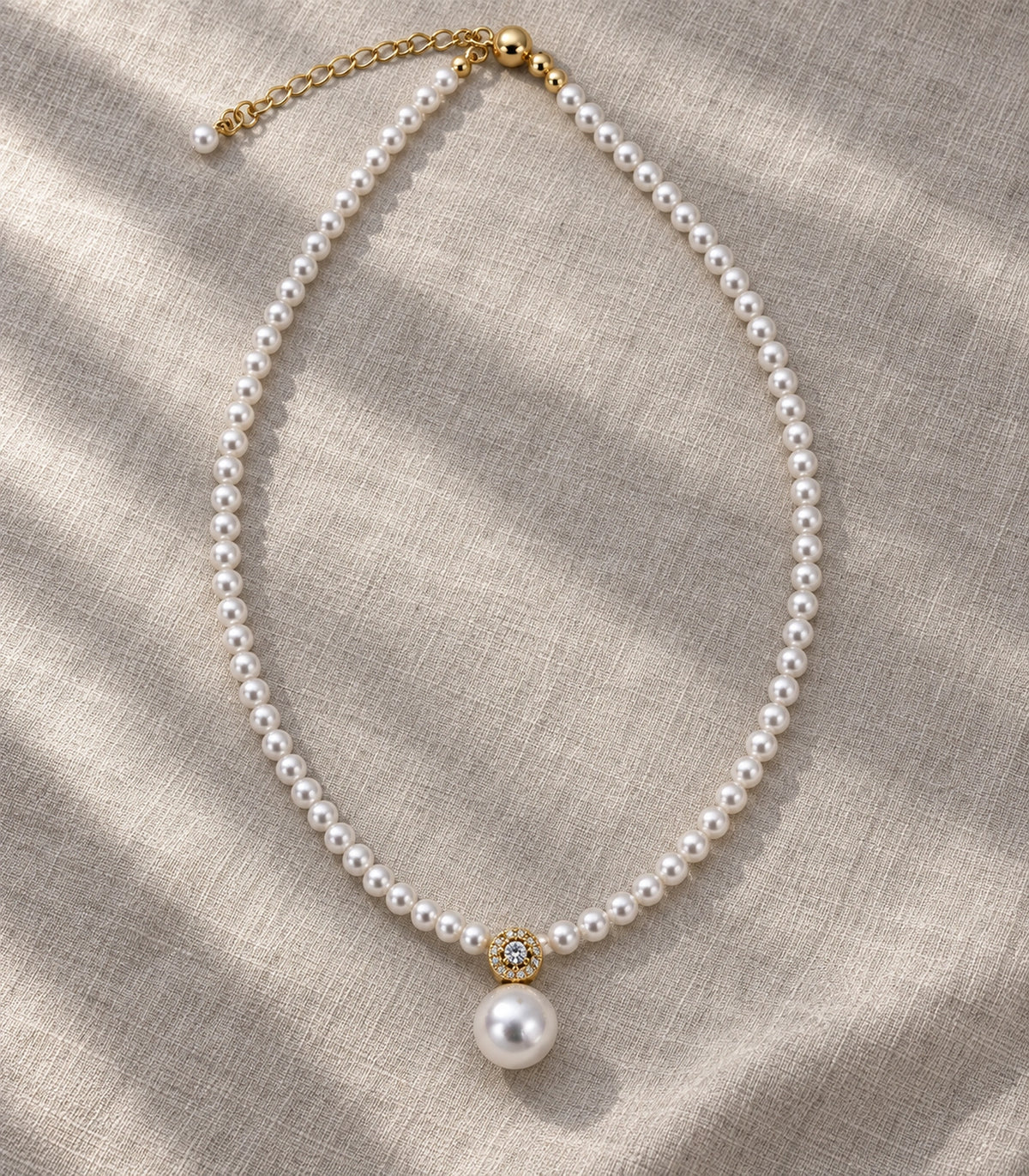 JIMIKI Gold Tone Crystal Rosette Pearl Drop Necklace in Gold / White, editorial flat lay