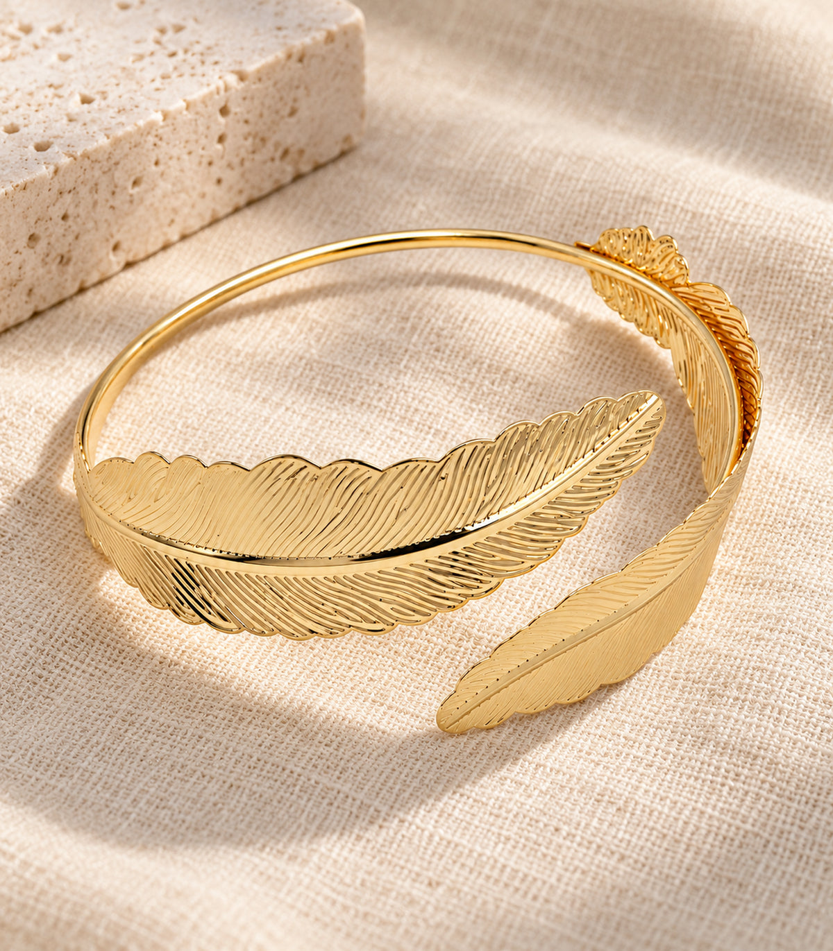 Single gold-tone double feather arm cuff arranged on linen and stone