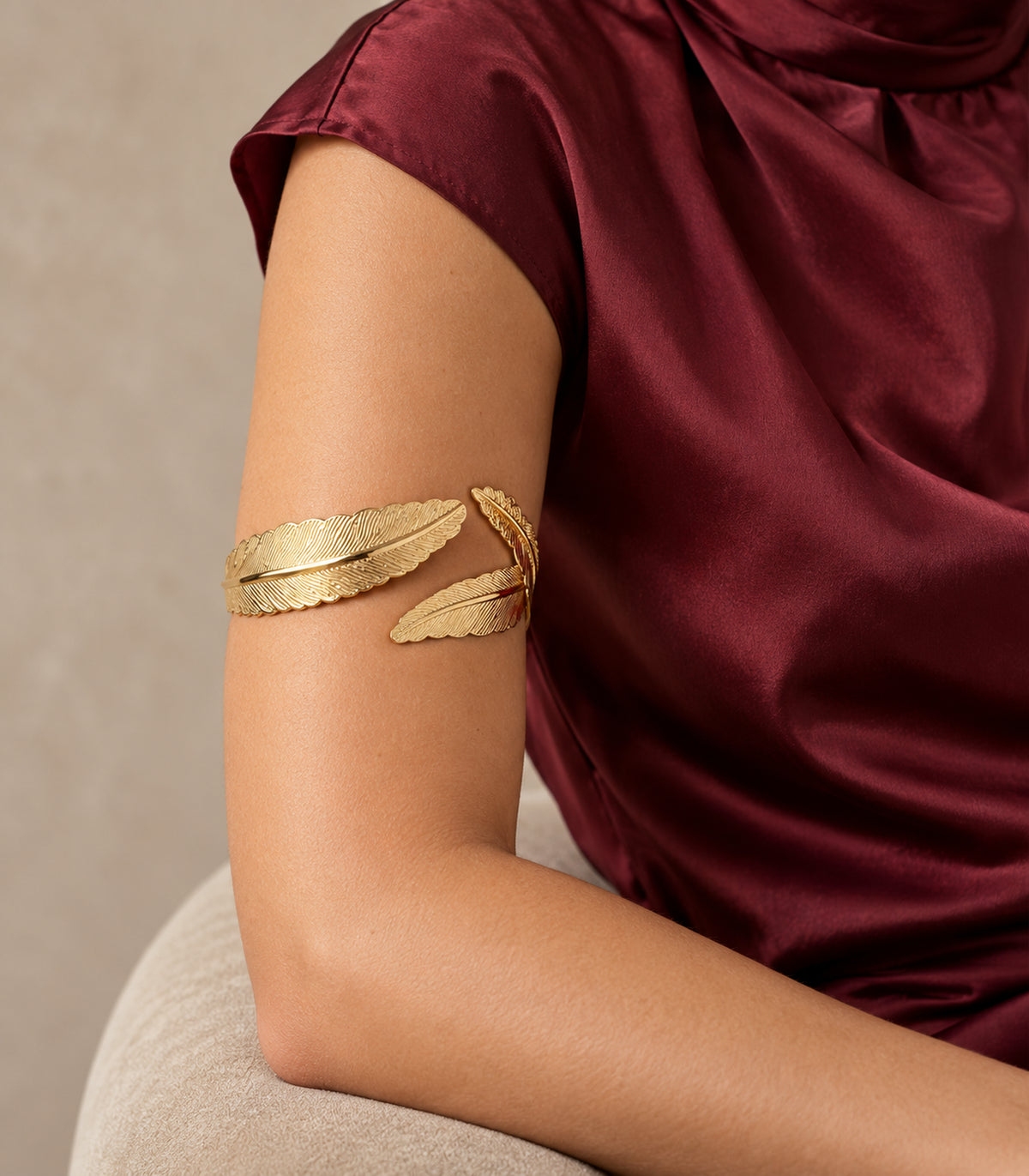 Gold-tone double feather cuff worn on the upper arm with burgundy clothing