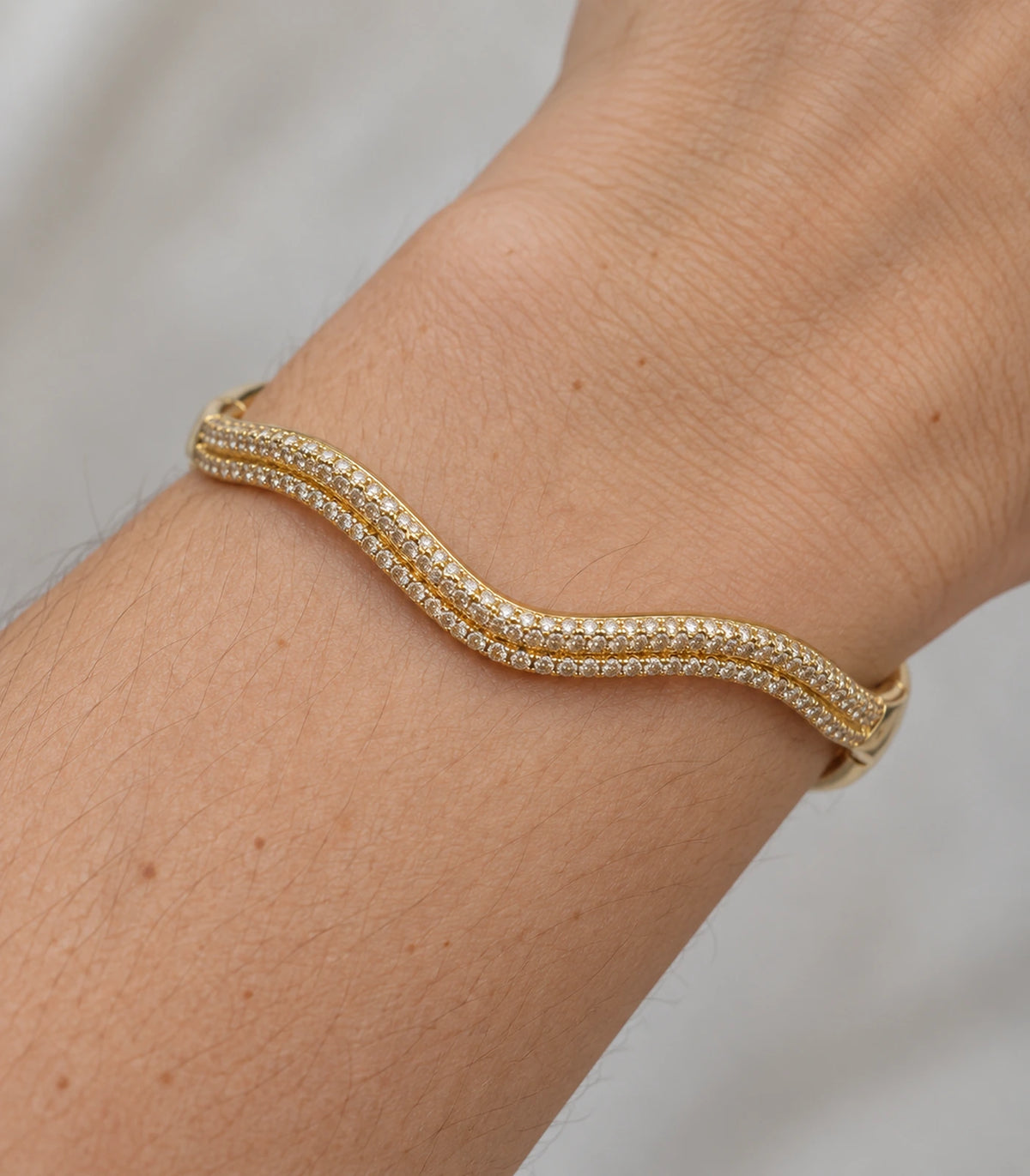 JIMIKI Gold-Tone Double Wave Pavé Bangle — close-up of the bangle worn on the wrist #color_gold-tone / clear