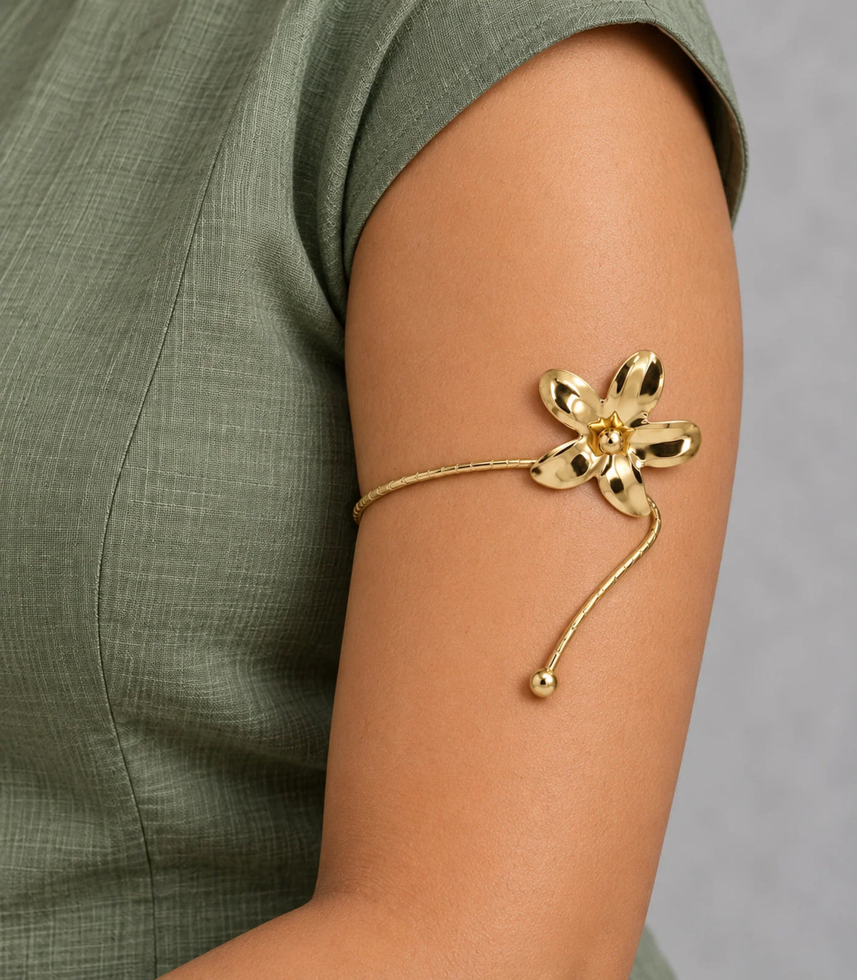 Worn closeup of gold-tone five-petal flower, bead and star centre, segmented band and ball-tip cuff with sage-green clothing