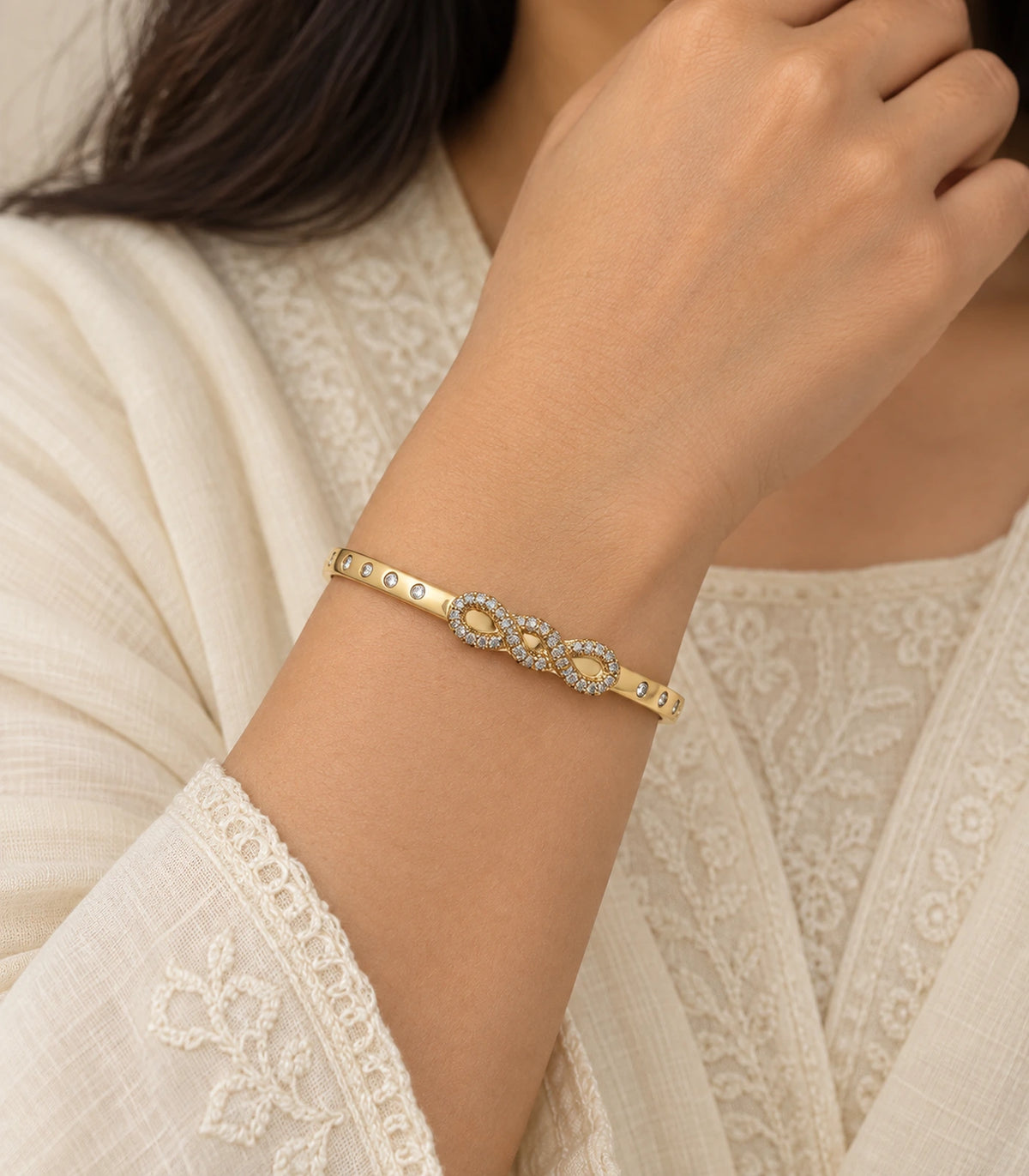 JIMIKI Gold-Tone Infinity Knot Bezel Stone Bangle — worn on the wrist #color_gold-tone / clear