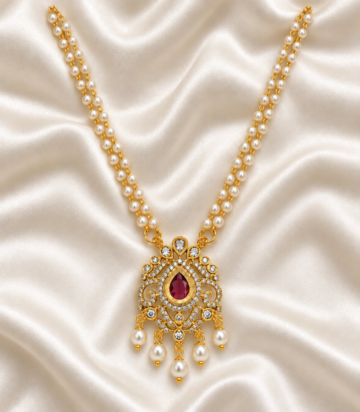 Single gold-tone magenta pendant necklace with twin white pearl-bead strands laid on ivory fabric; no earrings included.