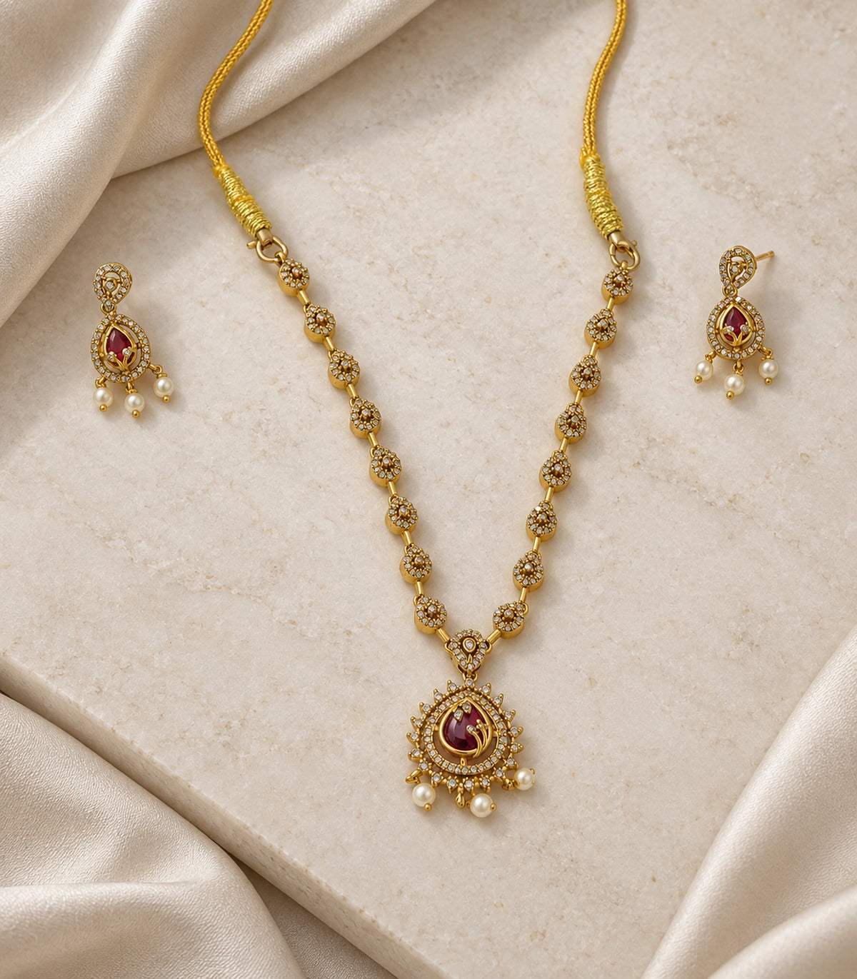 Magenta teardrop pendant necklace and matching earrings arranged on a light surface