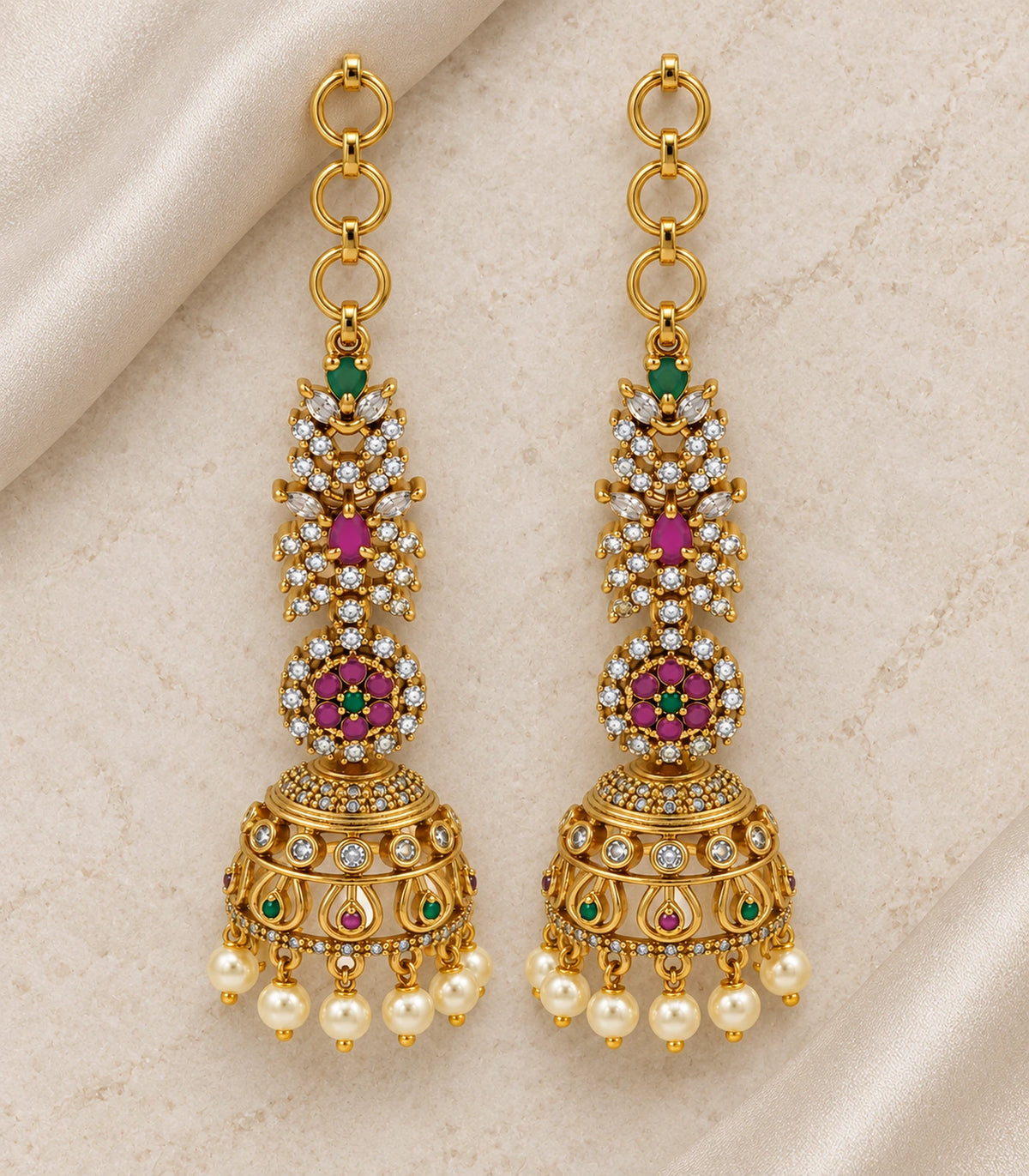 Matching gold-tone multicolor jhumka earring pair arranged on neutral fabric