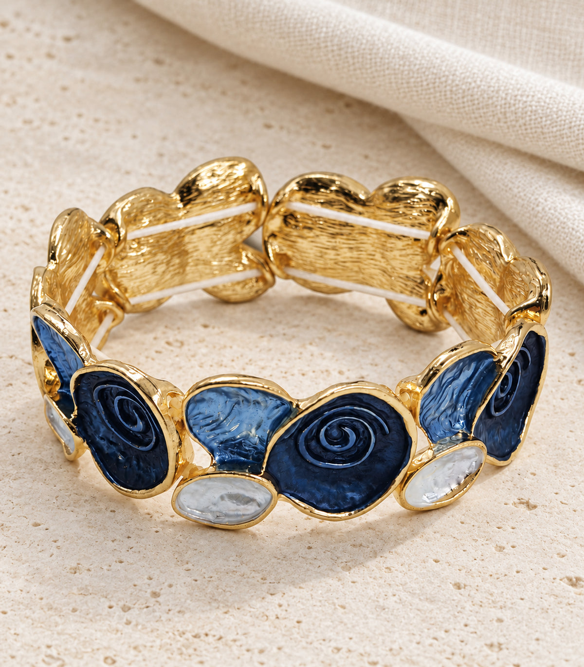 Gold-tone navy spiral and blue fan panel bracelet — editorial flatlay view