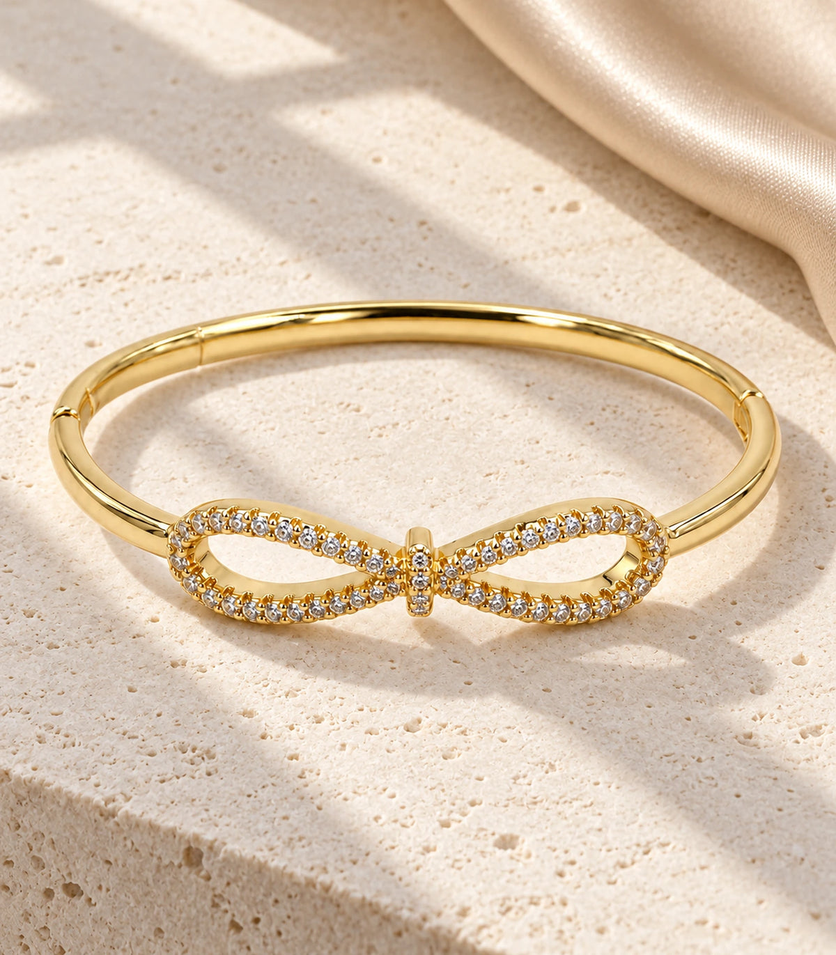 JIMIKI Gold-Tone Open Infinity Pavé Bangle — bangle in a styled flat lay #color_gold-tone / clear