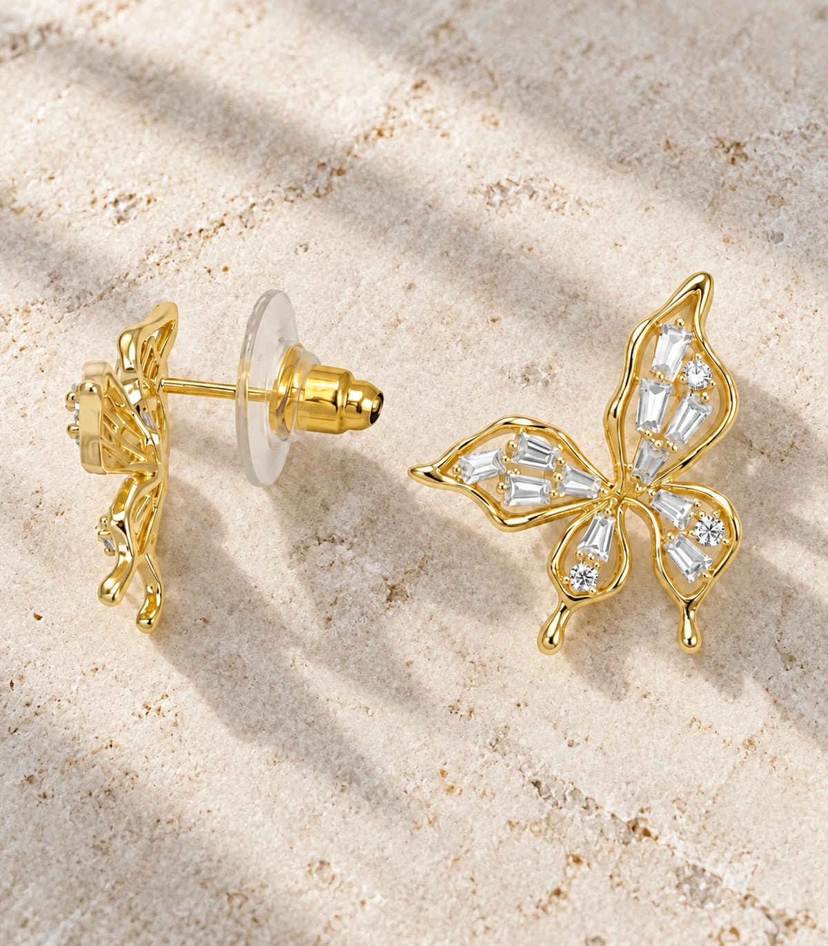 JIMIKI Openwork Baguette Crystal Butterfly Stud Earring Pair in Gold-tone, editorial flat lay #color_gold-tone