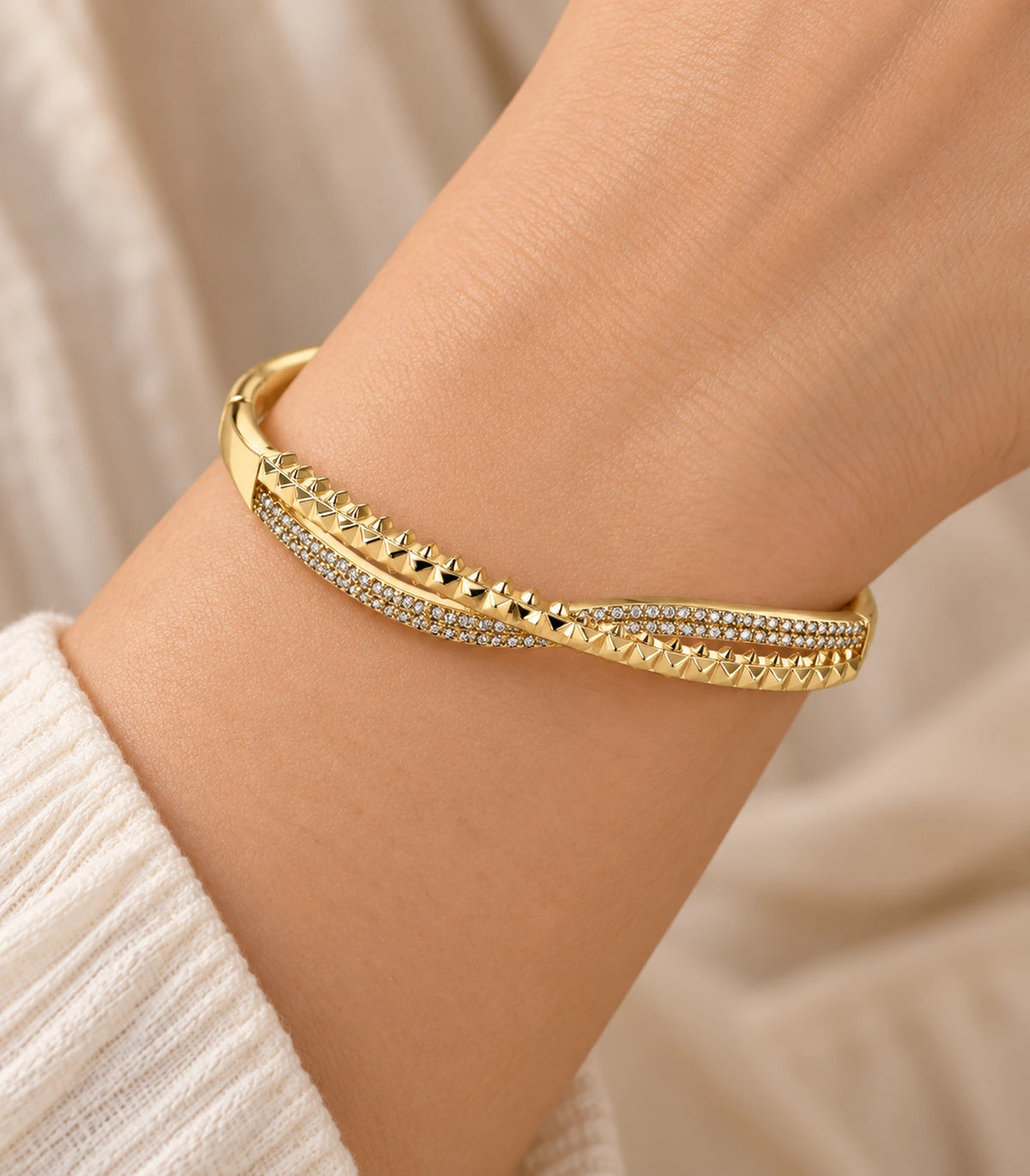 JIMIKI Gold-Tone Pavé Pyramid Crossover Bangle — close-up of the bangle worn on the wrist #color_gold-tone / clear