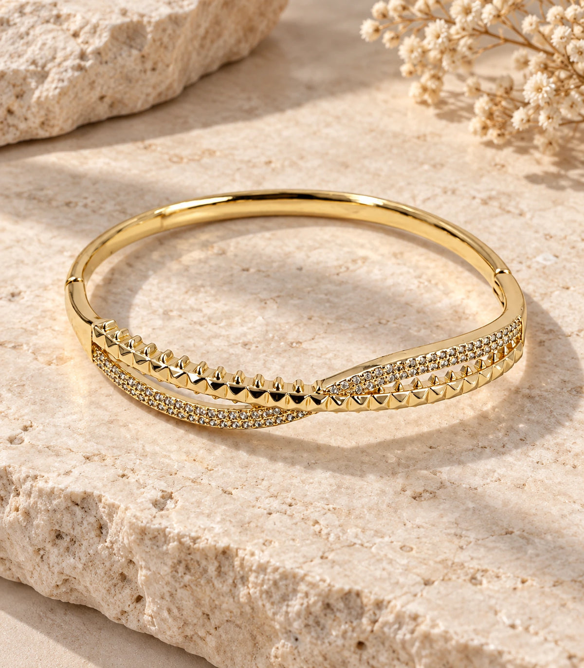 JIMIKI Gold-Tone Pavé Pyramid Crossover Bangle — bangle in a styled flat lay #color_gold-tone / clear