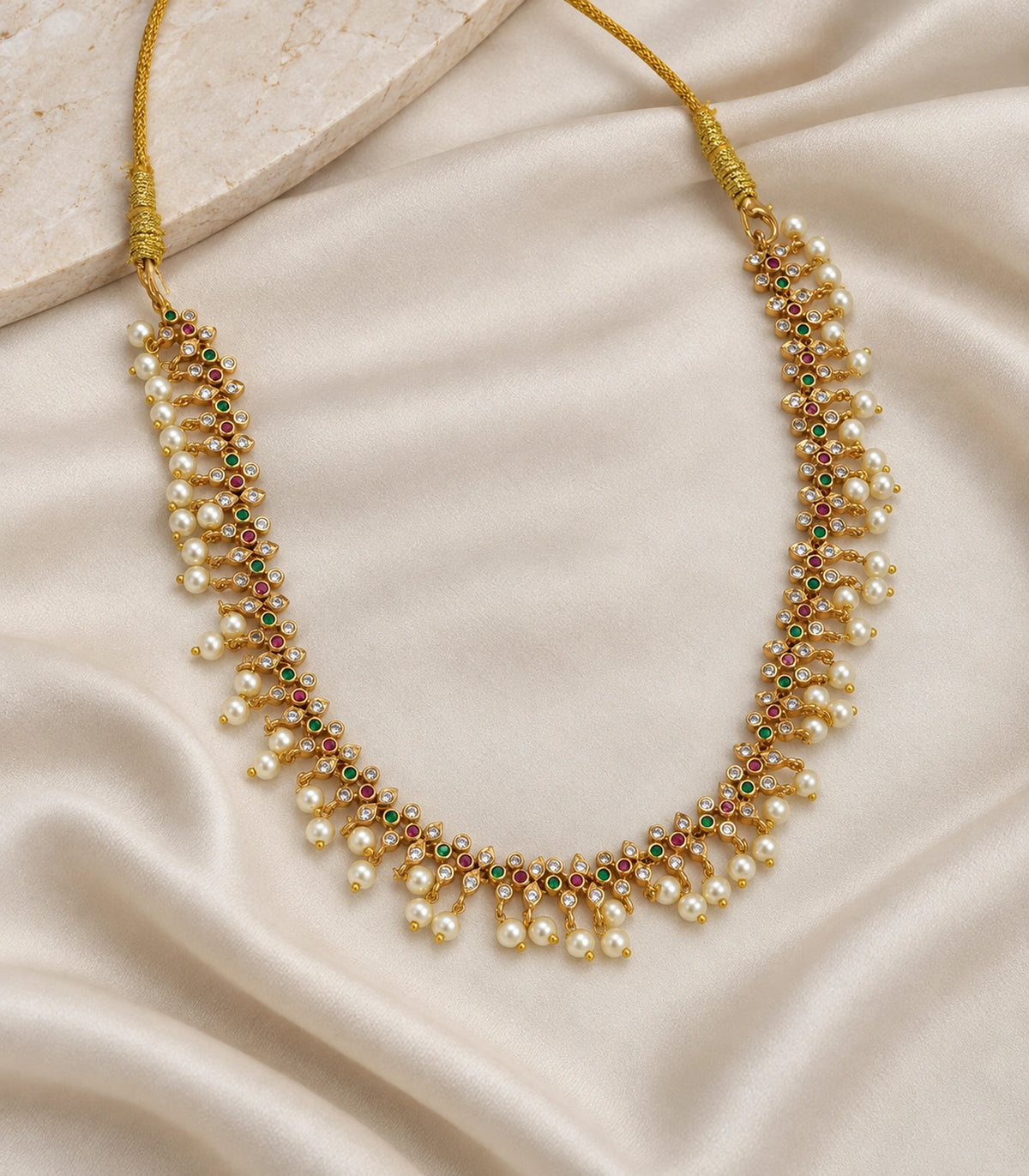 Gold-tone pearl lattice collar necklace arranged on light fabric