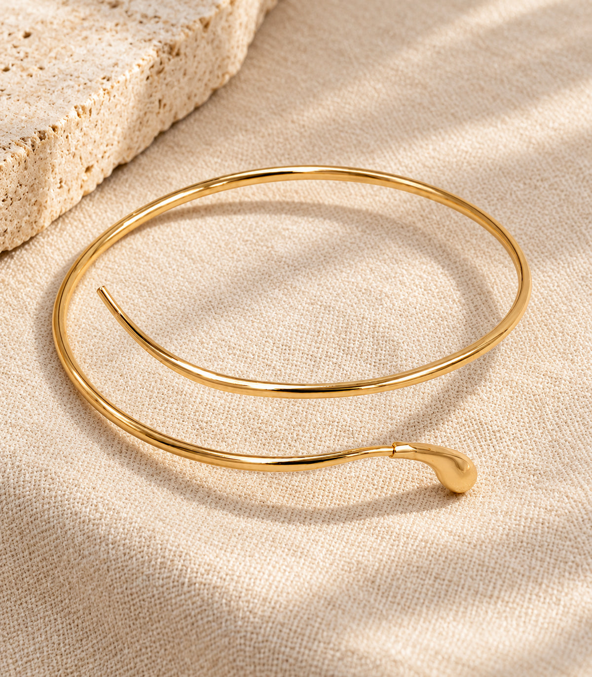 Single gold-tone teardrop tip open arm cuff displayed complete on neutral linen