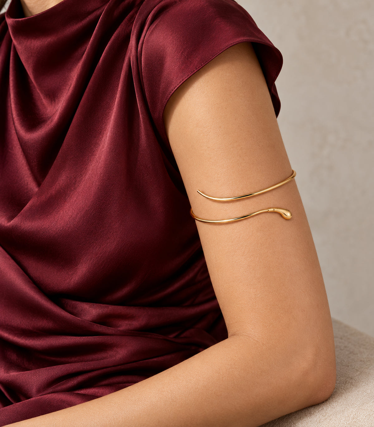 Gold-tone teardrop tip open arm cuff worn on the upper arm with burgundy styling