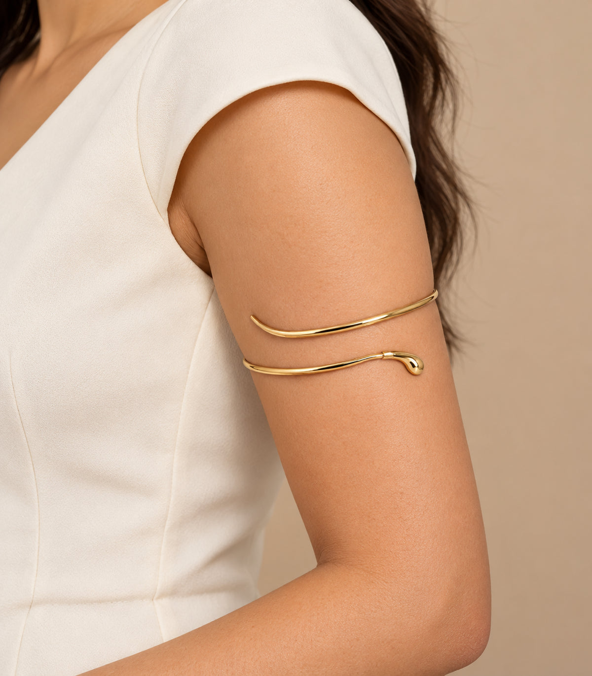 Gold-tone teardrop tip open arm cuff worn on the upper arm with an ivory blouse