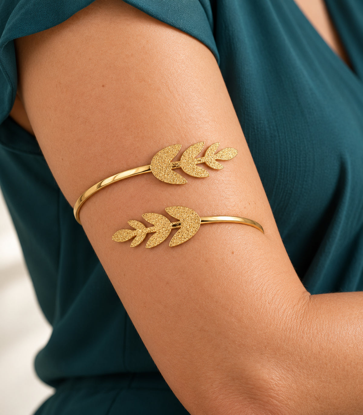 Close view of the gold-tone textured double leaf sprig cuff worn on the upper arm
