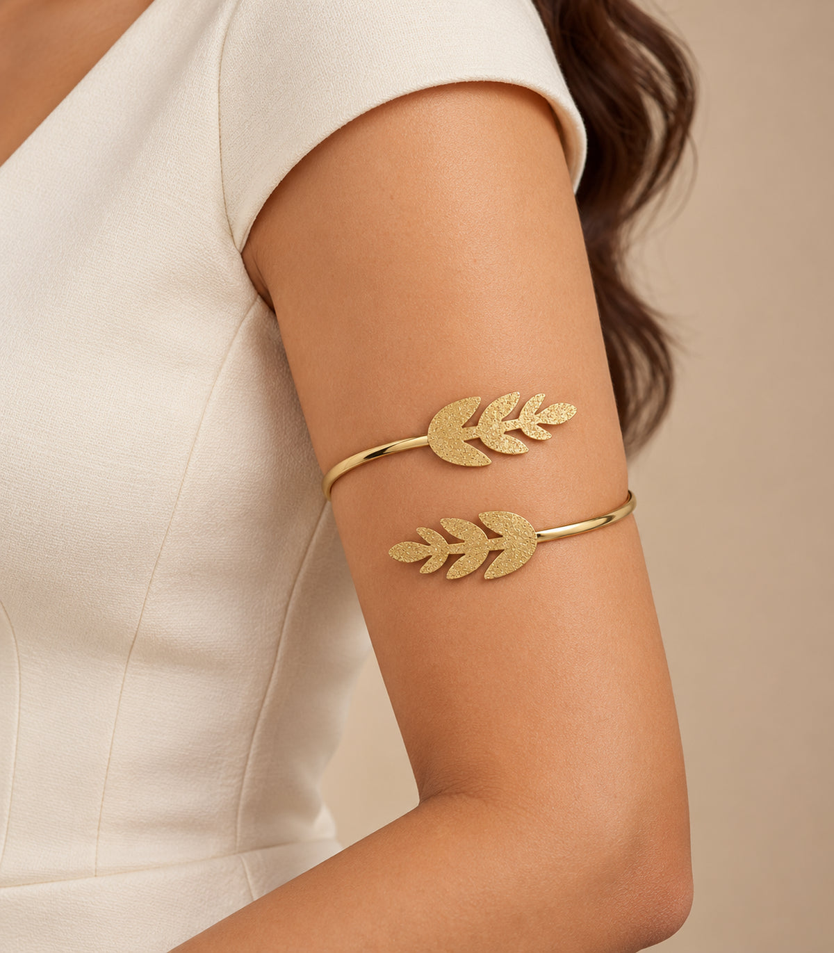 Gold-tone double leaf sprig cuff worn on the upper arm with ivory clothing