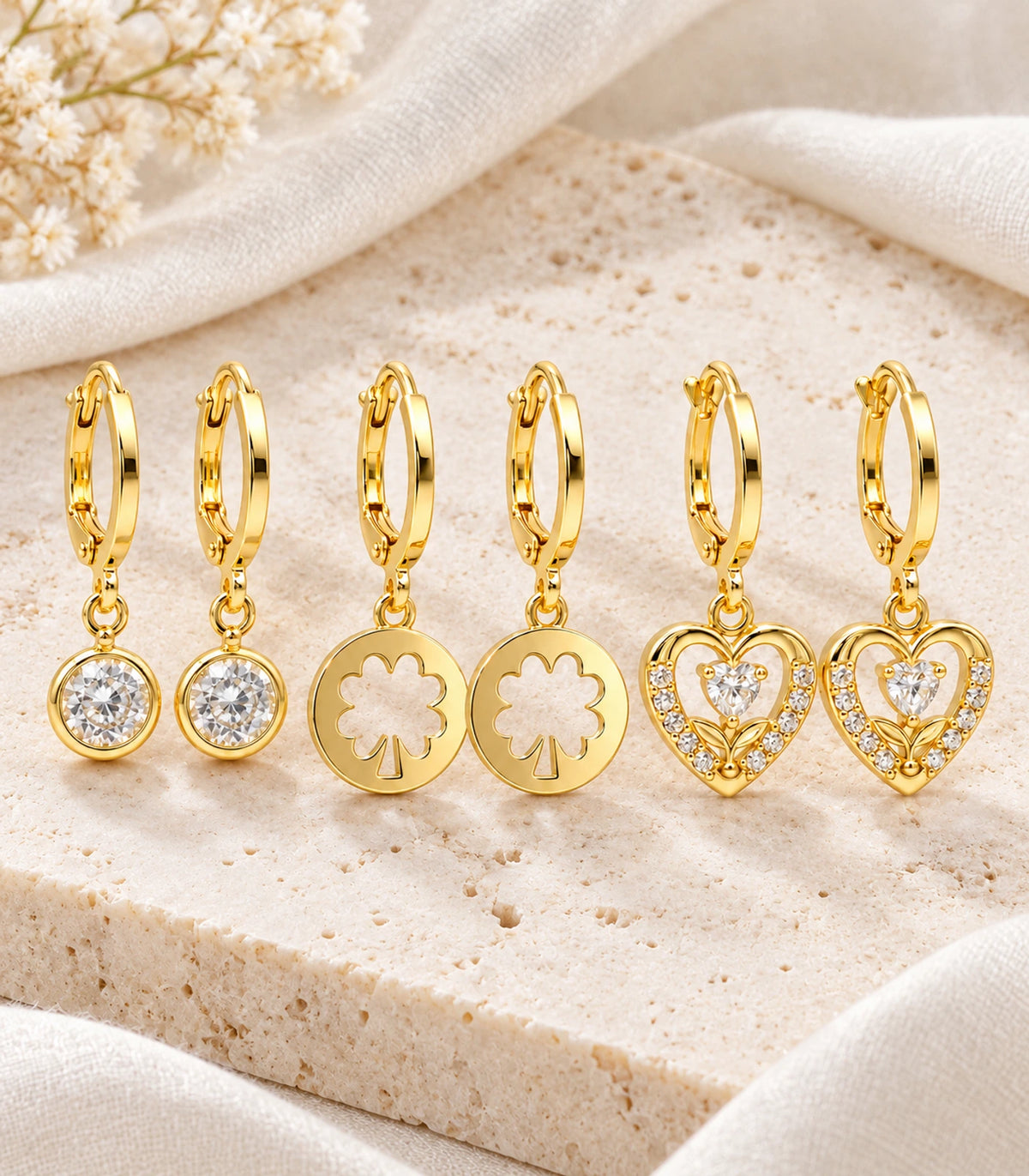 Complete gold-tone three-pair crystal, clover cutout and heart hoop earring set in editorial flat lay