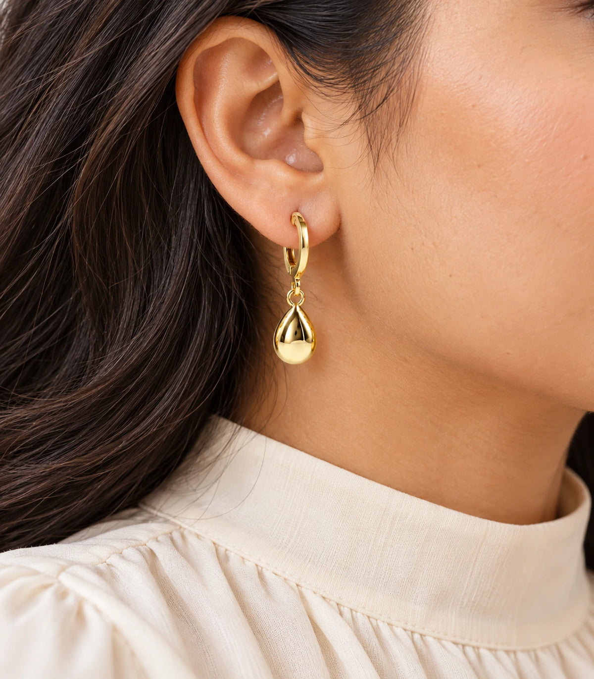 Gold tone puffed teardrop hoop earring worn close up