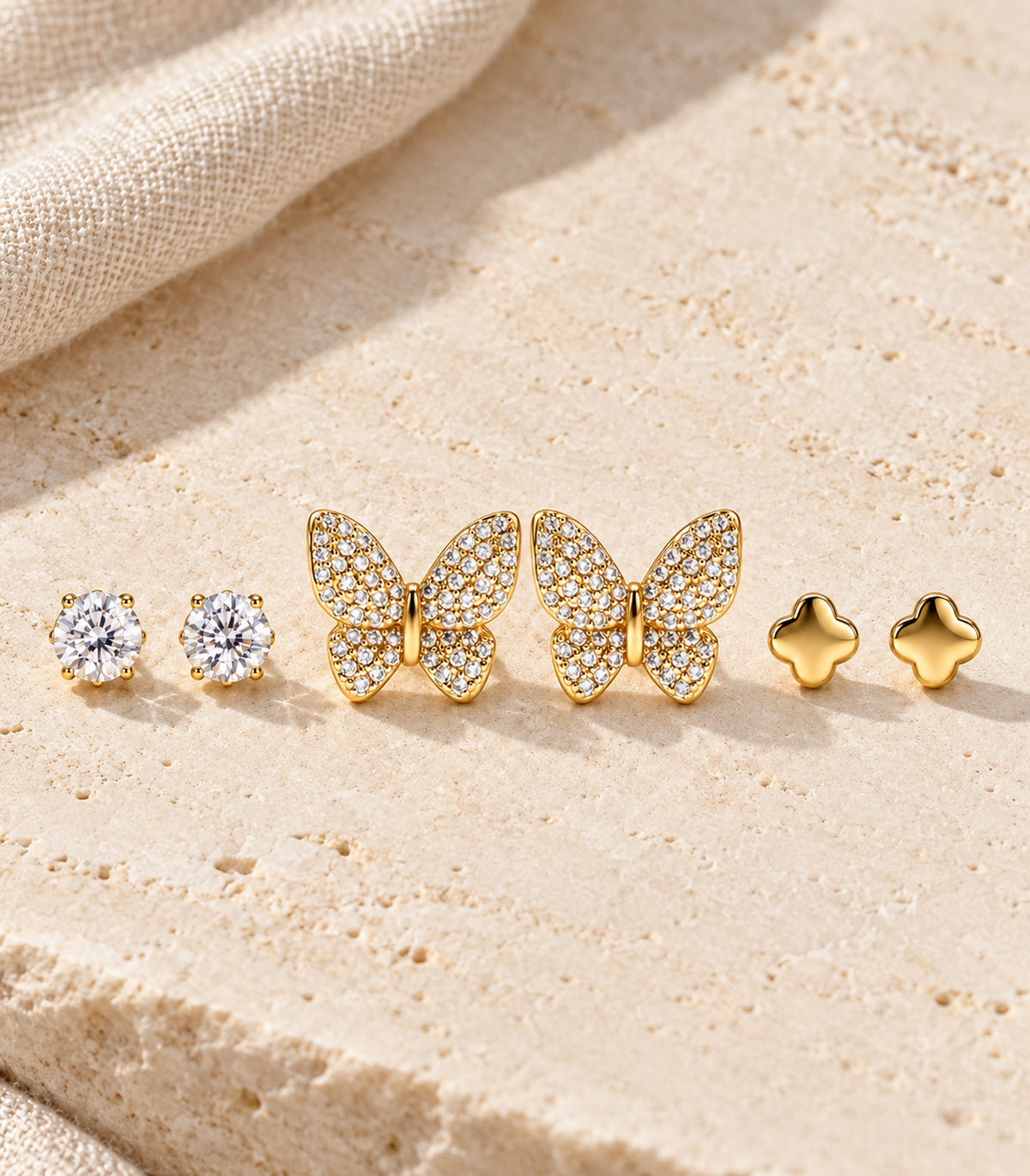 All six gold-tone studs arranged as three matching pairs on a pale limestone surface.