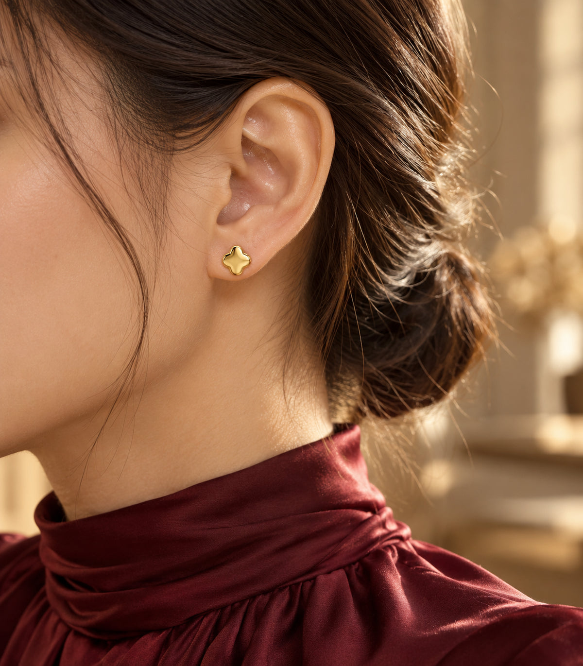 One small polished four-lobed gold-tone flower stud from the three-pair set worn on an earlobe.