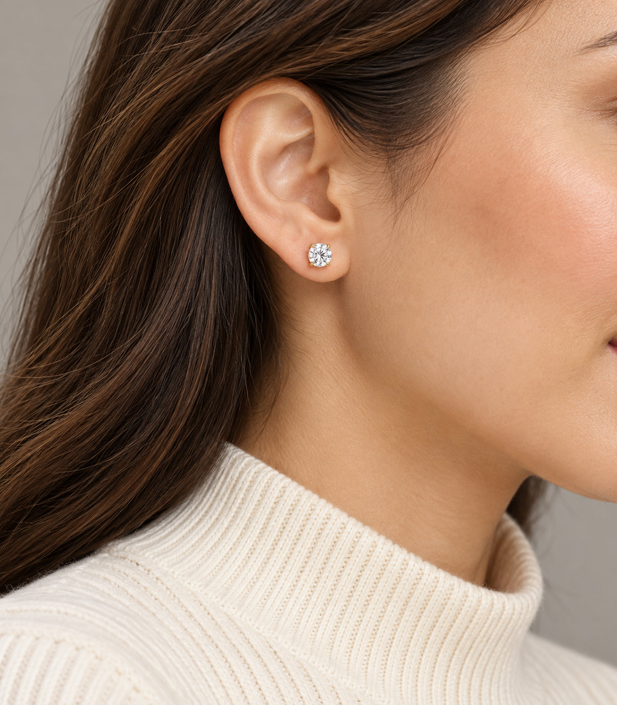 One clear round crystal stud from the three-pair gold-tone set worn on an earlobe.