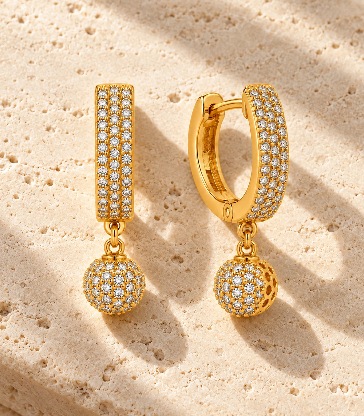 JIMIKI Gold-Tone Three-Row Pavé Ball Drop Huggie Earrings — pair in a styled flat lay #color_gold-tone / clear