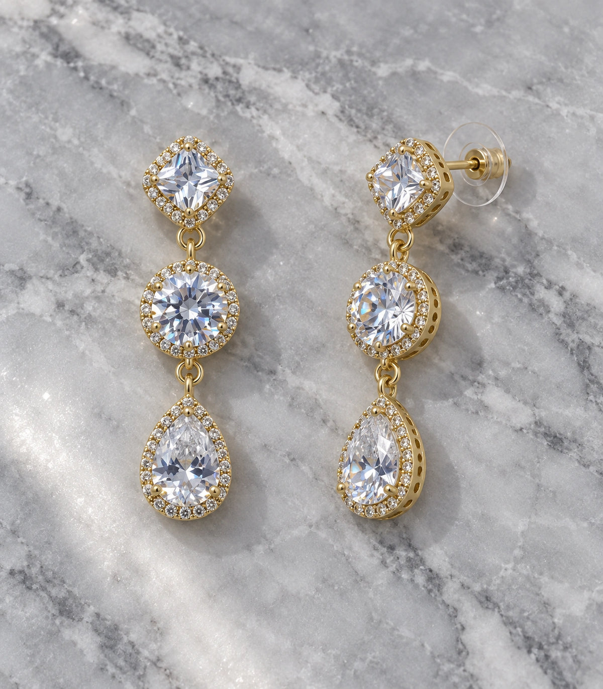 JIMIKI Gold-Tone Three-Stone Halo Drop Earrings in Gold / Clear, editorial flat lay