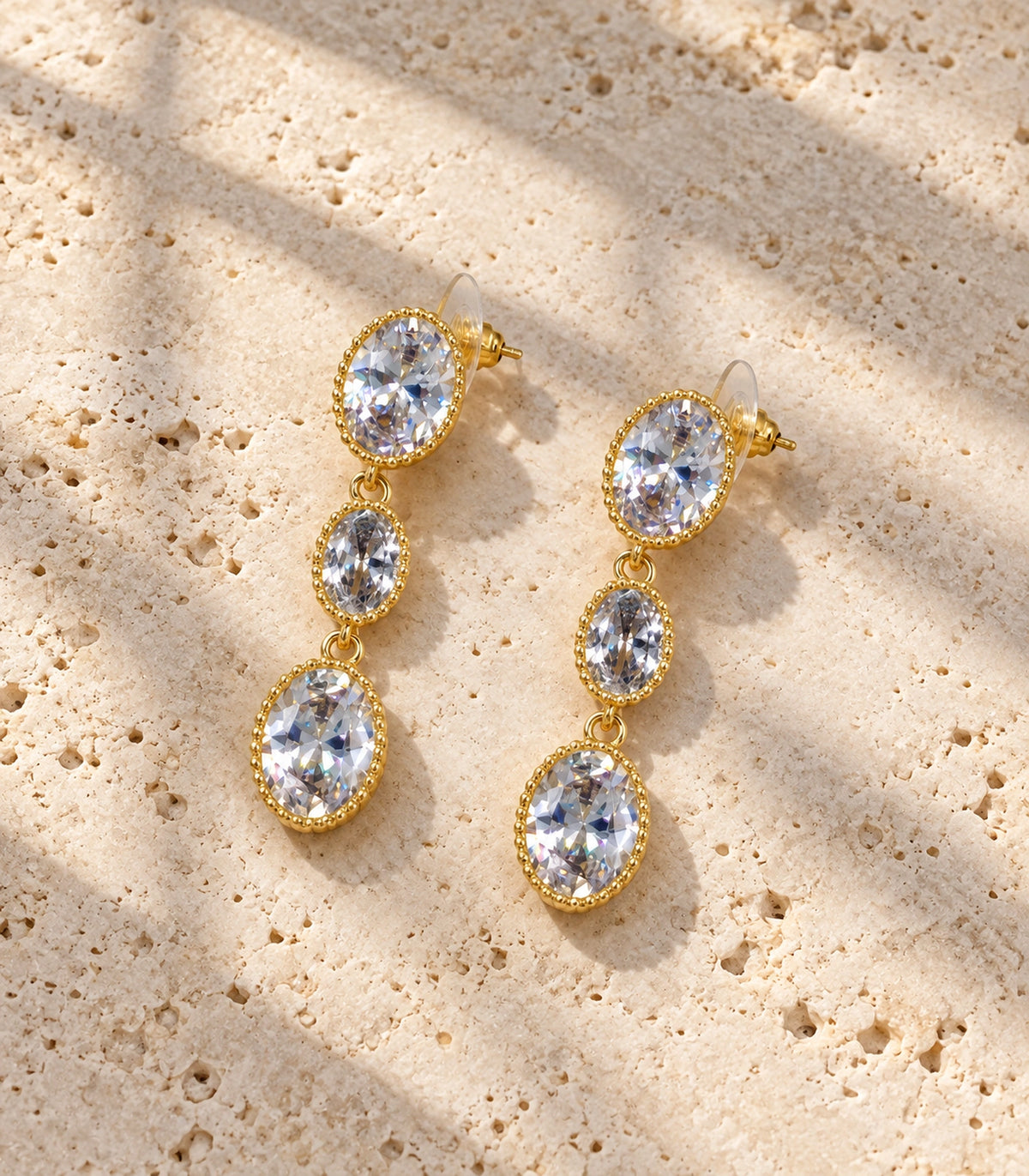 JIMIKI Triple Oval Crystal Drop Earrings in Gold Tone, editorial flat lay #color_gold tone