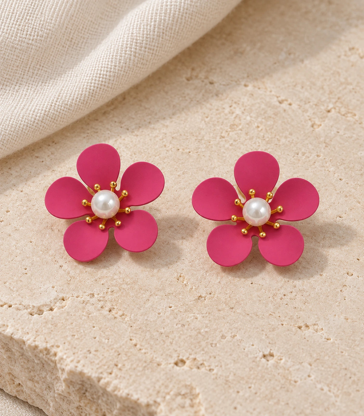 JIMIKI hot pink five-petal flower stud earrings with pearl-effect centre, matching flower stud pair in an editorial flat lay #color_hot-pink