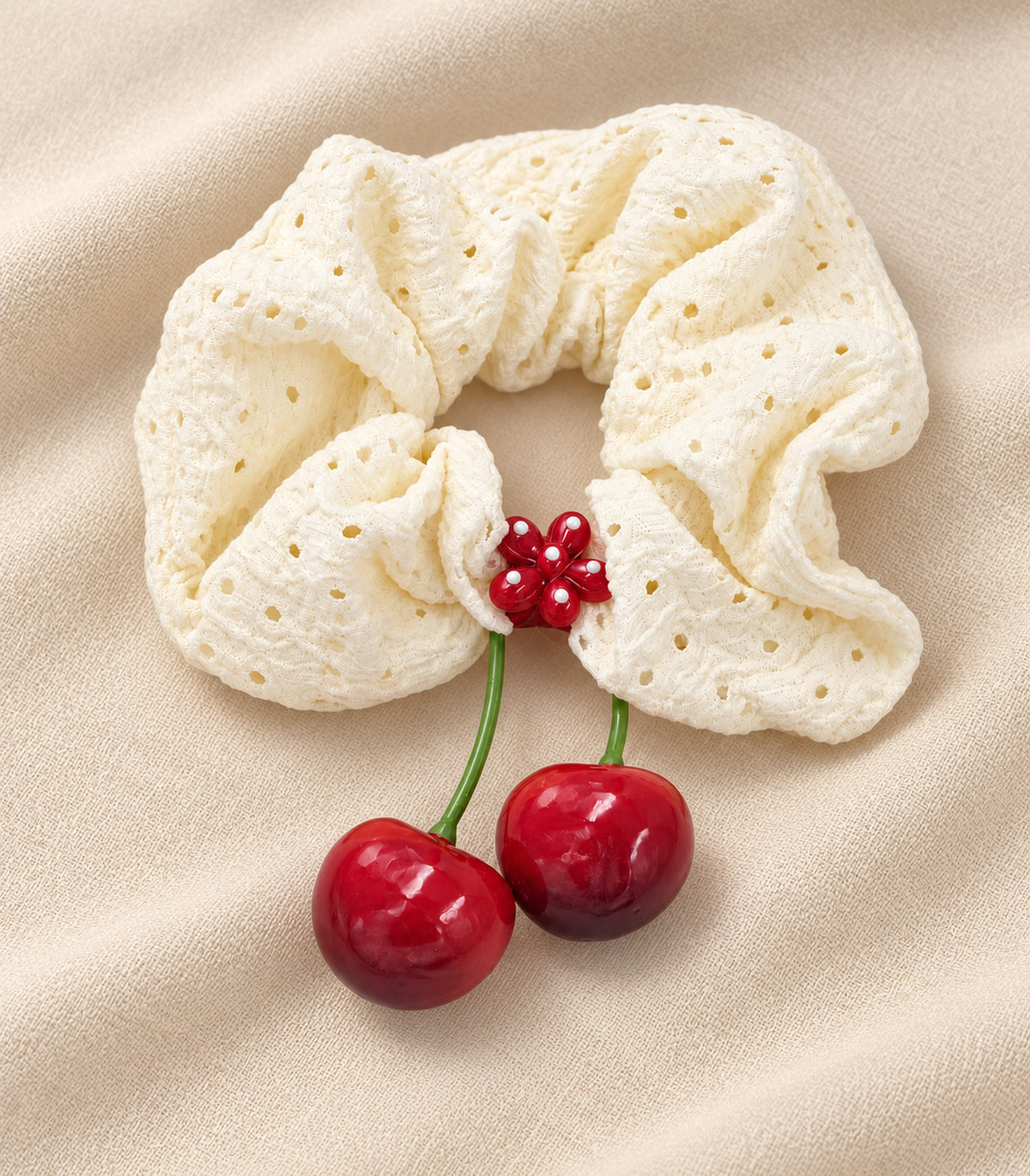 Ivory eyelet cherry scrunchie with dotted red flower centre — editorial flatlay view