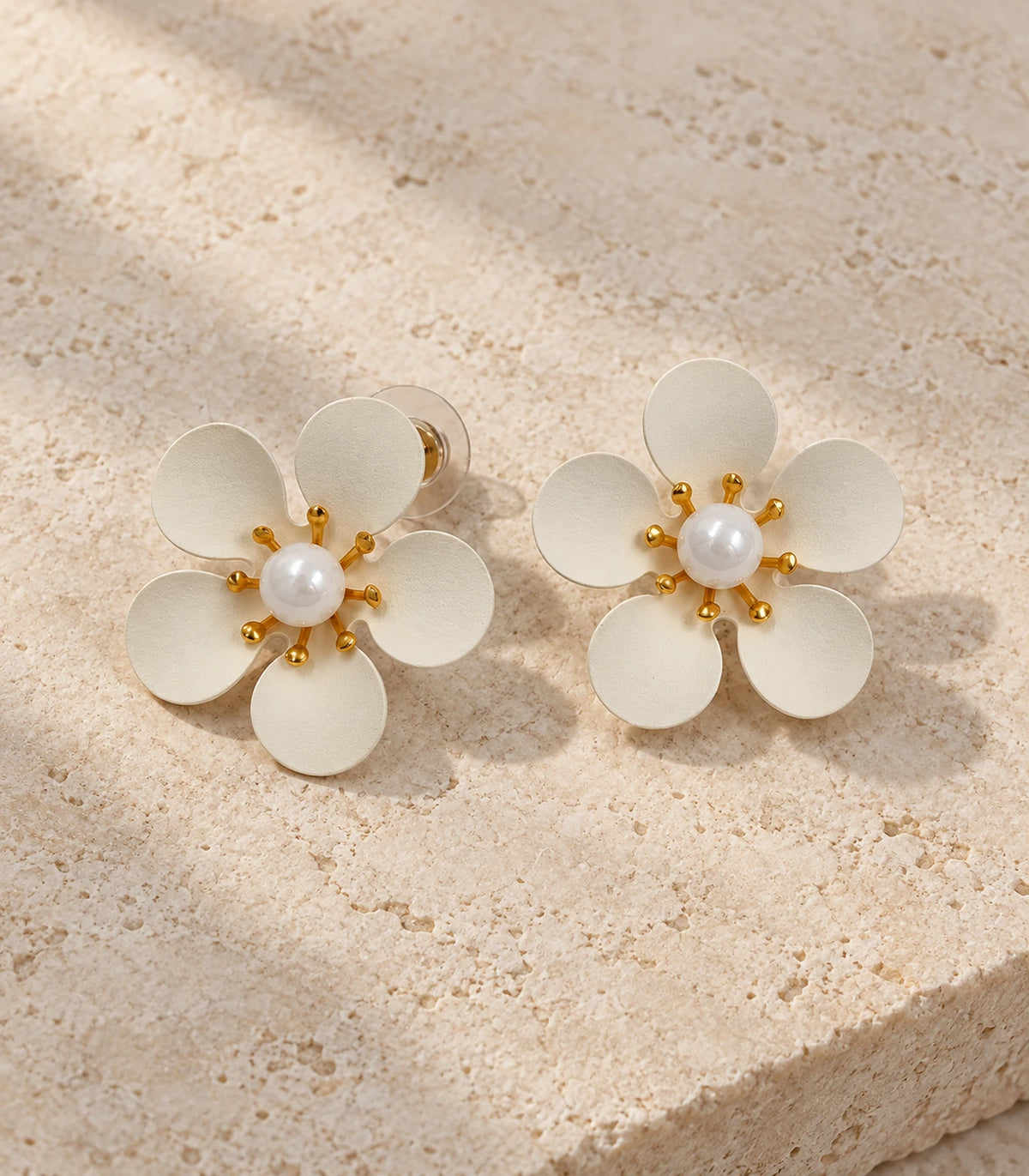JIMIKI ivory five-petal flower stud earrings with pearl-effect centre, matching pair on pale stone #color_ivory