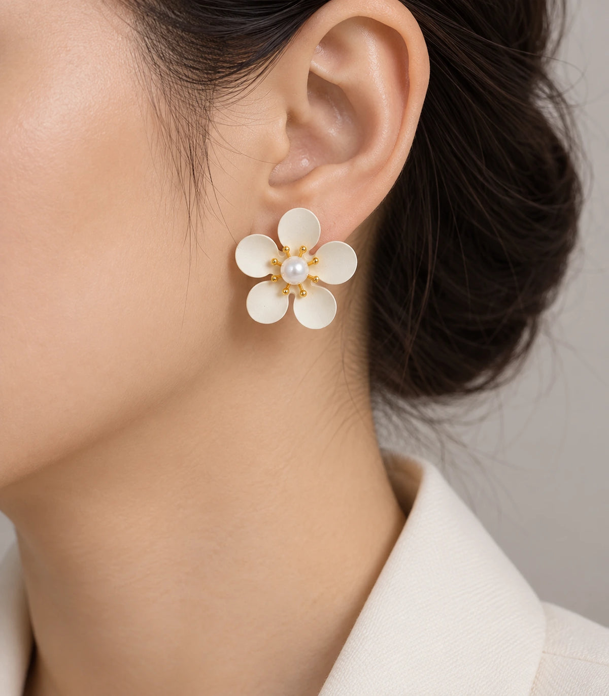 JIMIKI ivory five-petal flower stud earrings with pearl-effect centre, stud worn with swept-back hair #color_ivory