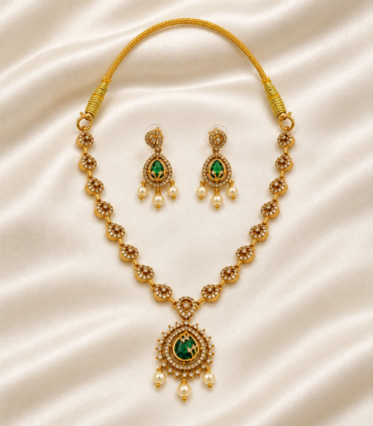 Complete gold-tone green necklace and matching earring pair arranged on ivory silk