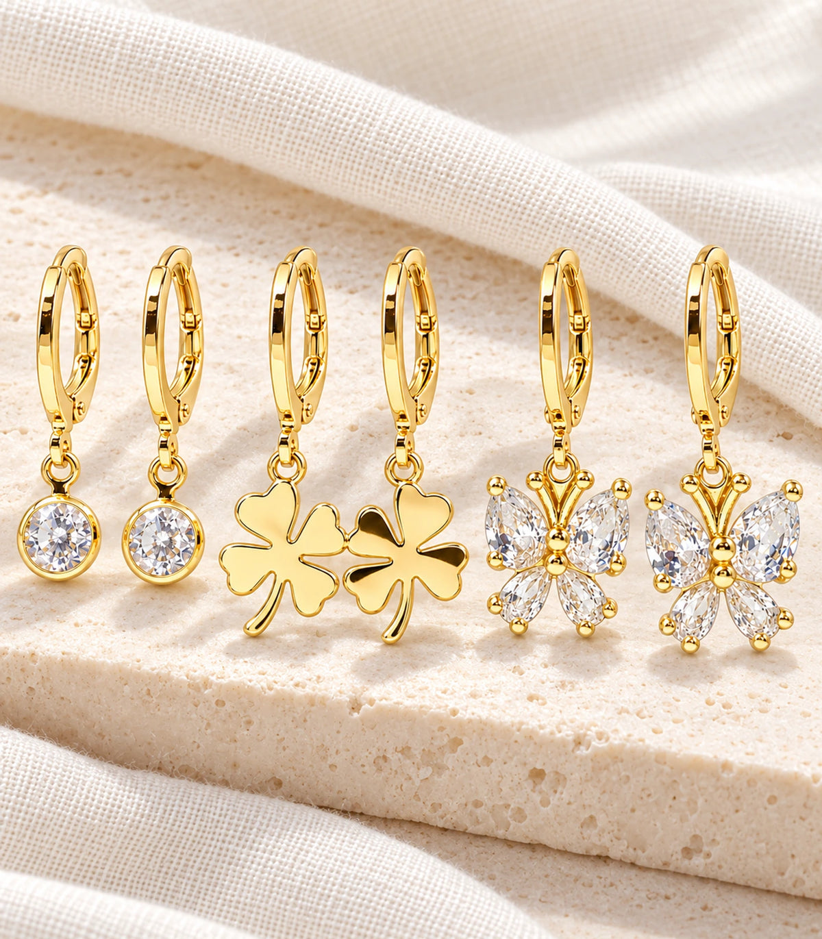 Complete gold-tone three-pair crystal, clover and butterfly hoop set on ivory fabric; six earrings
