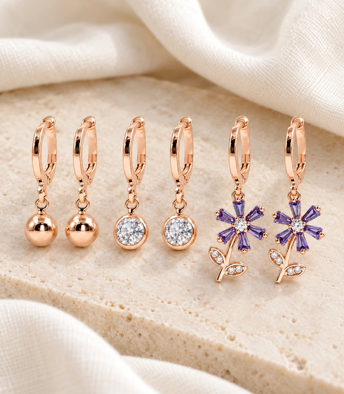 JIMIKI rose gold tone three-pair ball, crystal and purple flower hoop earring set — editorial-flatlay