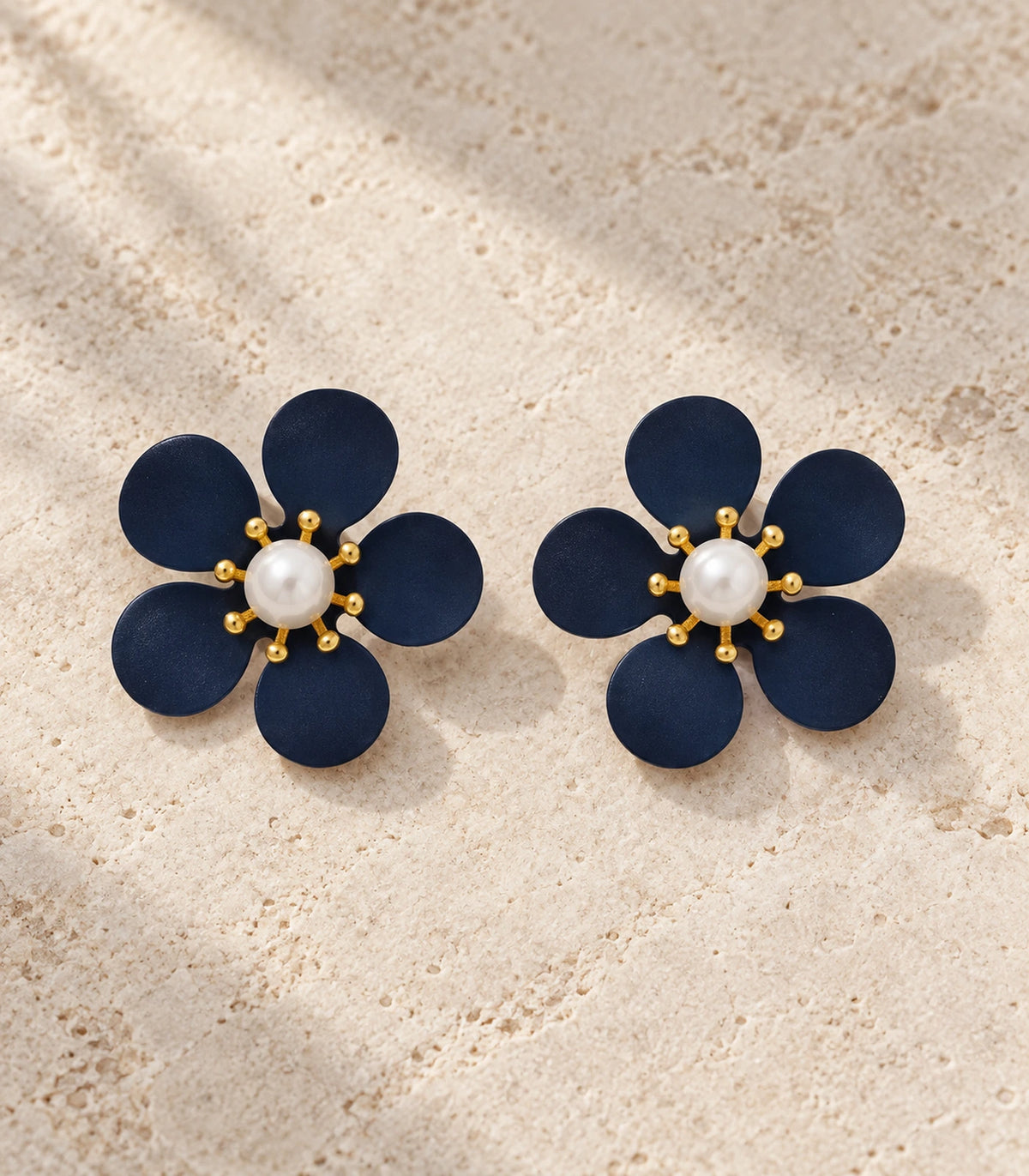 JIMIKI navy five-petal flower stud earrings with pearl-effect centre, matching flower stud pair in an editorial flat lay #color_navy