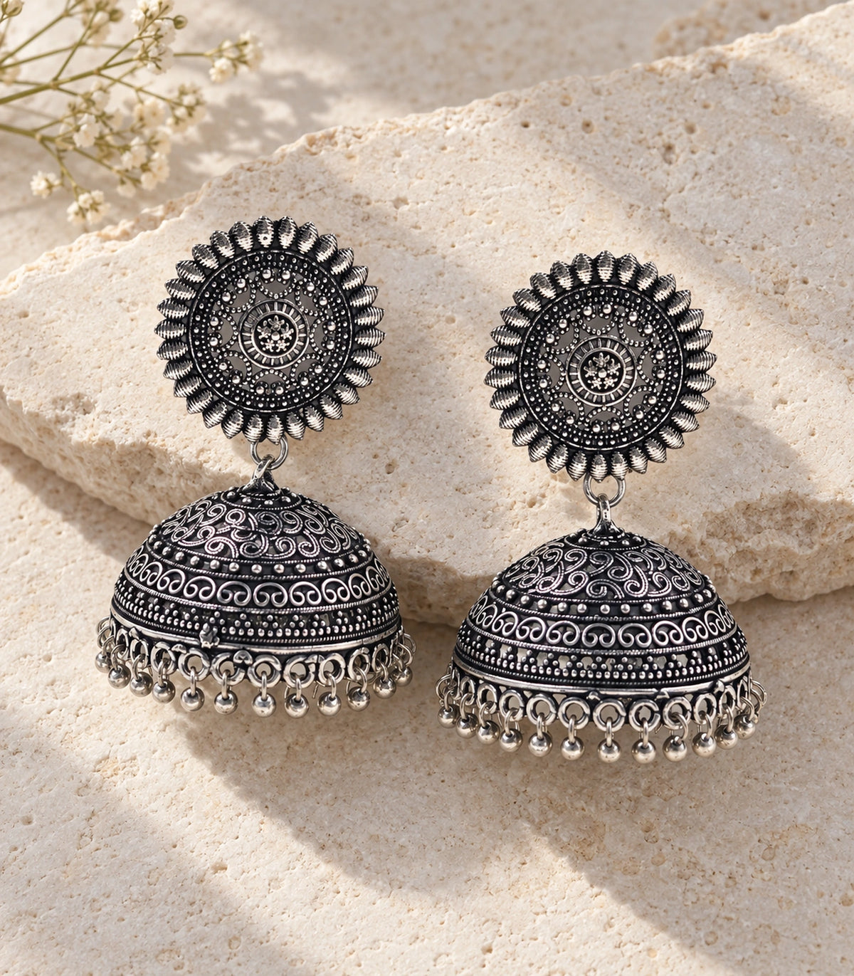 JIMIKI Oxidized Silver Sunburst Scroll Dome Jhumka Earrings - styled flatlay of the matching earrings #color_oxidized-silver