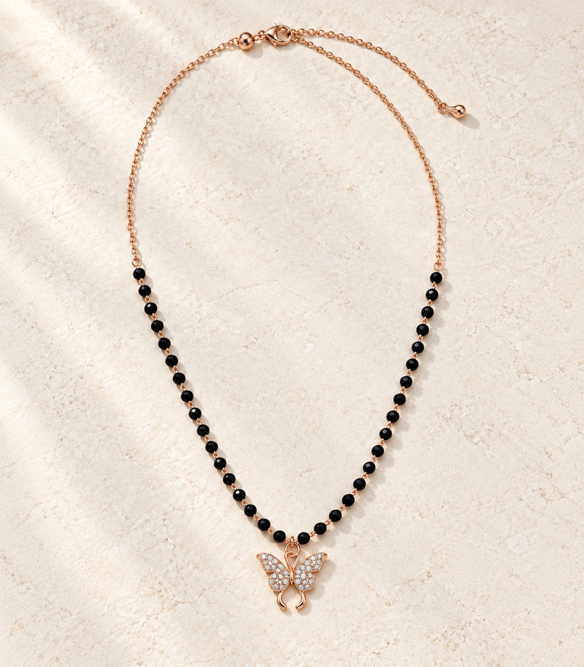 JIMIKI Rose-Gold Black-Bead Crystal Butterfly Necklace in Rose Gold / Black - editorial flatlay #color_rose-gold-black