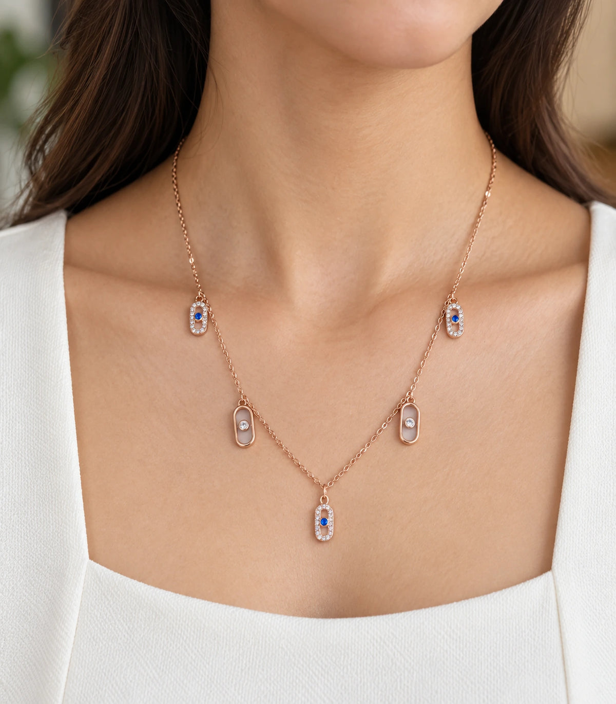 JIMIKI Rose Gold Blue Clear Oval Station Necklace - worn closeup of blue and clear oval drops #color_rose-gold