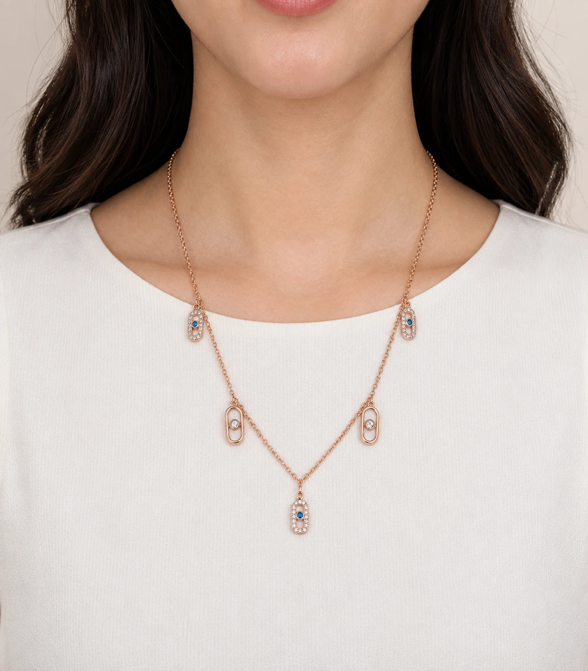 JIMIKI Rose Gold Blue Clear Oval Station Necklace - oval station necklace worn against an ivory top #color_rose-gold