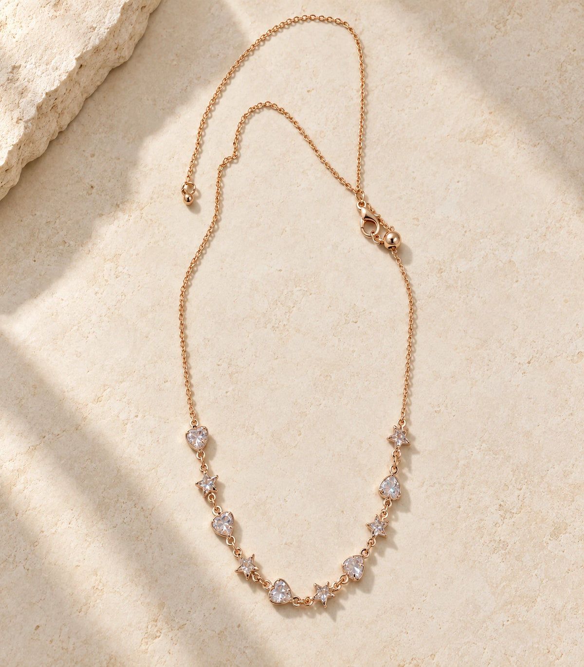 JIMIKI Rose Gold Crystal Heart Star Station Necklace - complete heart and star necklace in a styled flat lay #color_rose-gold