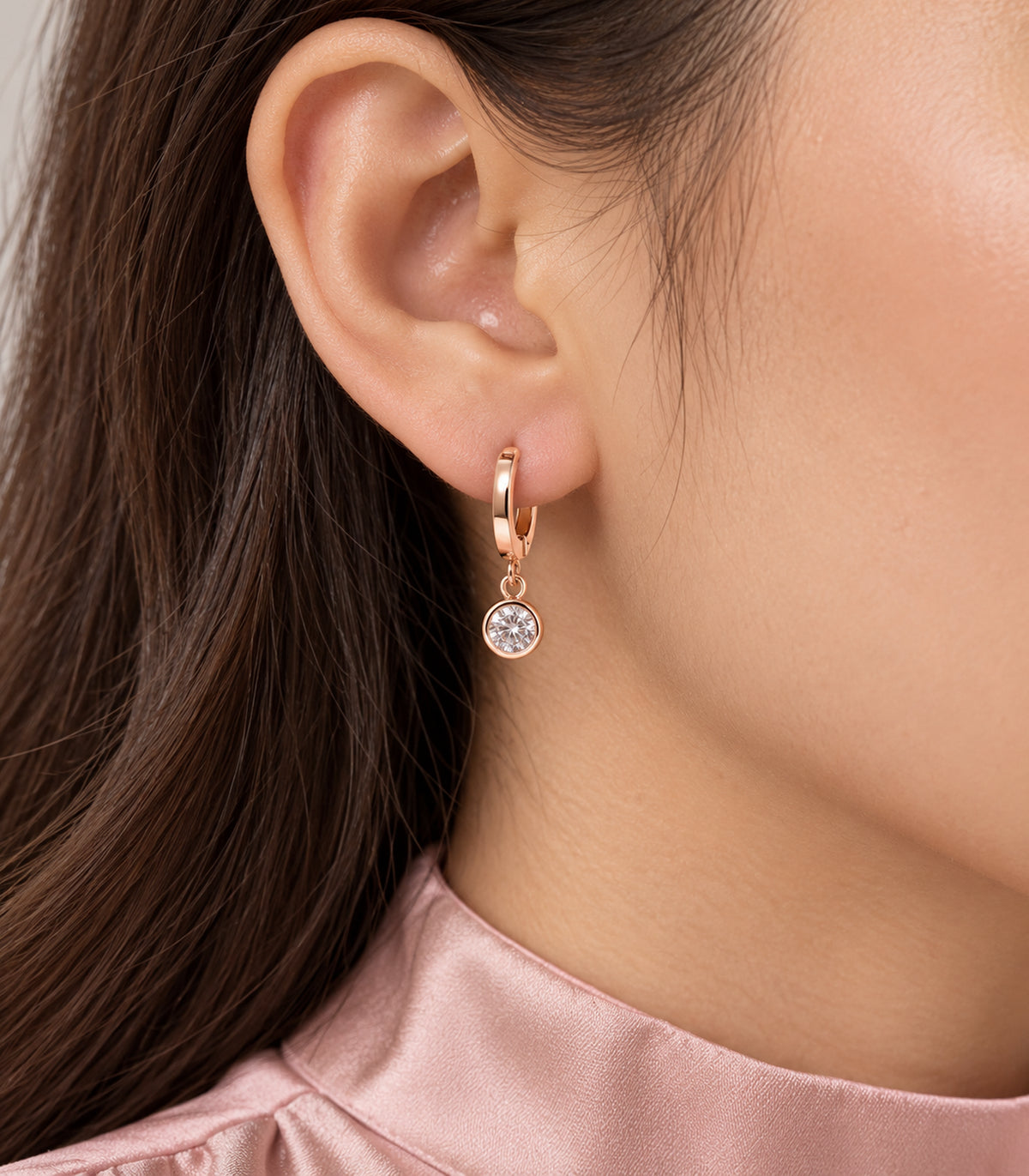 Round clear crystal-style bezel drop on a rose gold tone hoop worn close up