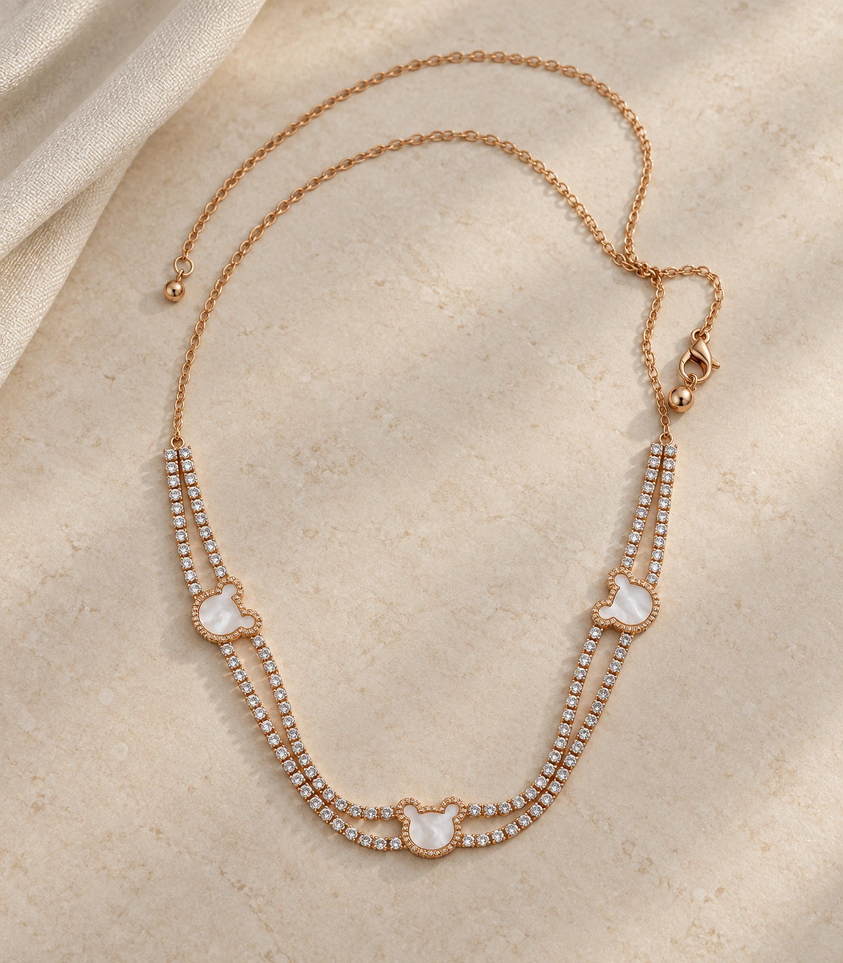 JIMIKI rose-gold-tone double-strand motif necklace, necklace styled flat on a light textured surface #color_rose gold