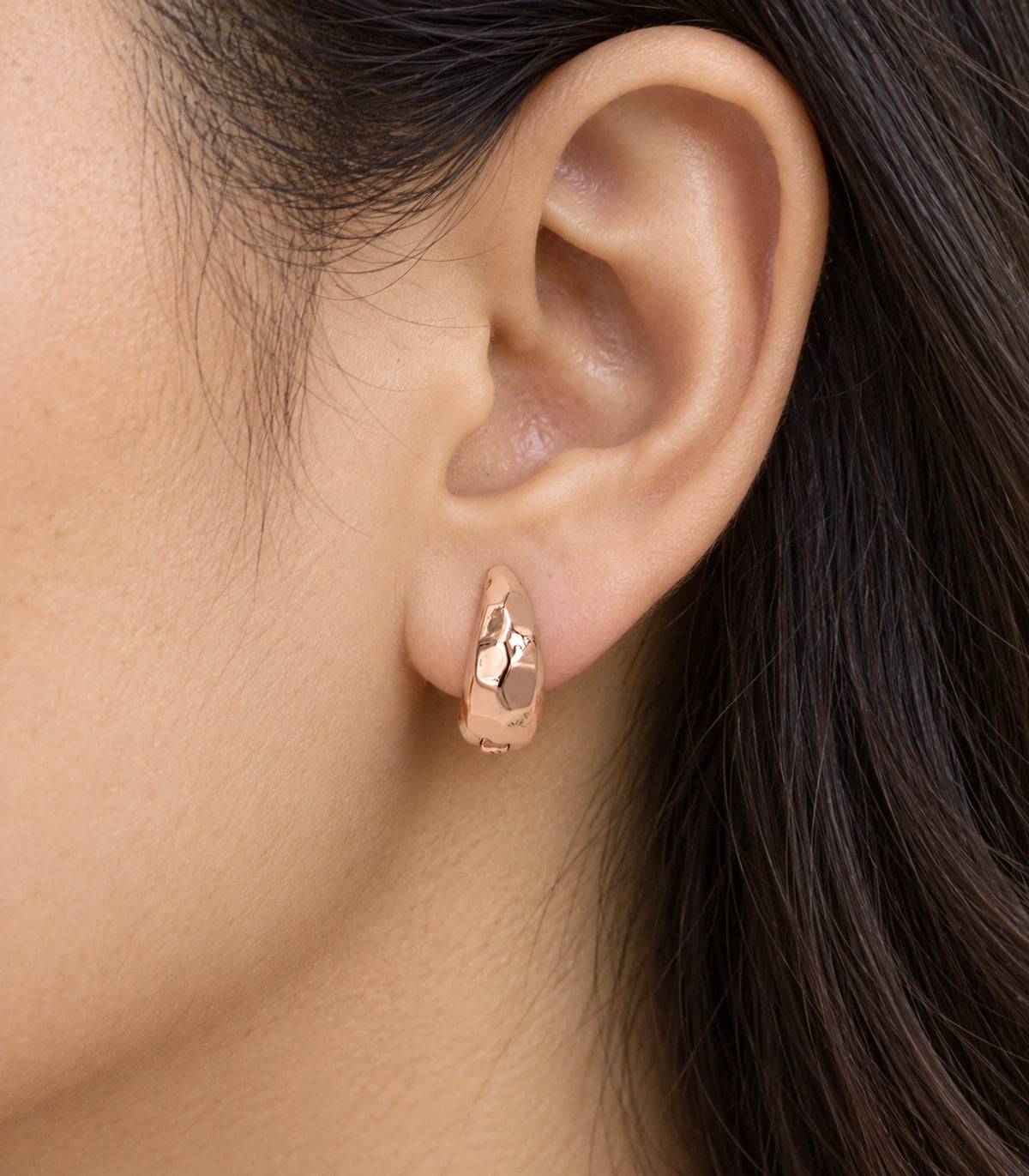 JIMIKI rose gold faceted huggie hoop earrings, worn closeup of the front design #color_rose-gold-tone