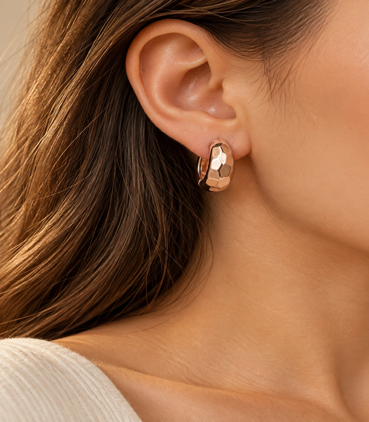 JIMIKI rose gold faceted huggie hoop earrings, worn in warm editorial lighting #color_rose-gold-tone