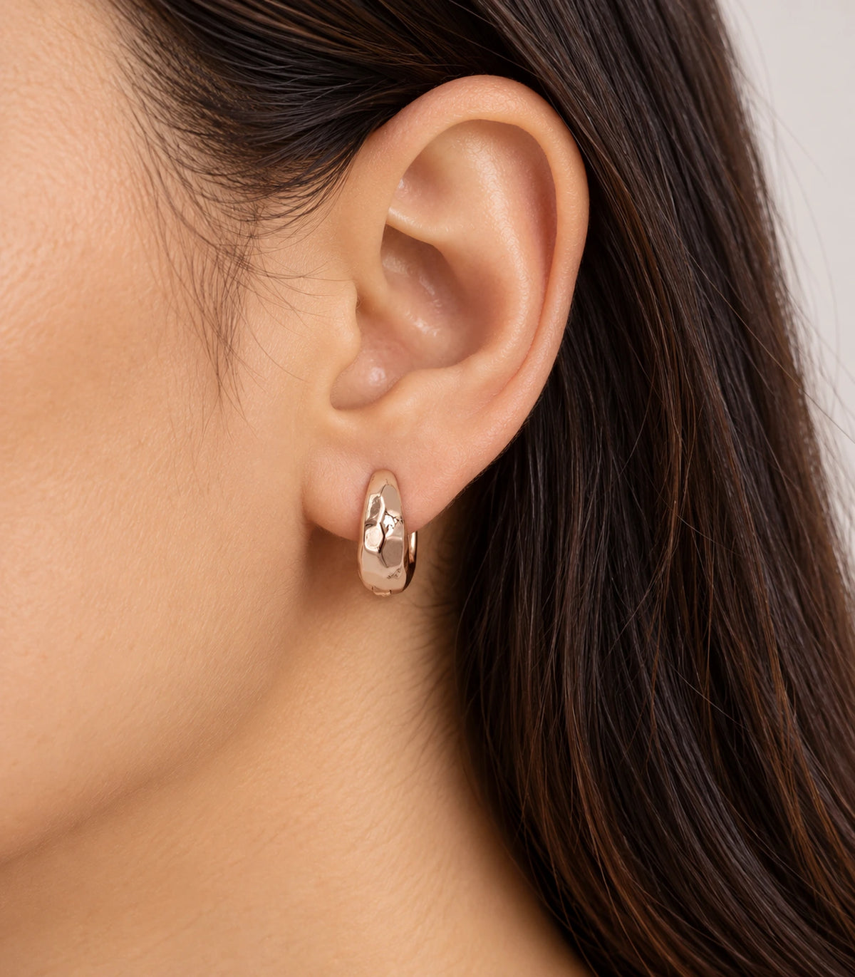 JIMIKI rose gold faceted huggie hoop earrings, worn on the ear #color_rose-gold-tone