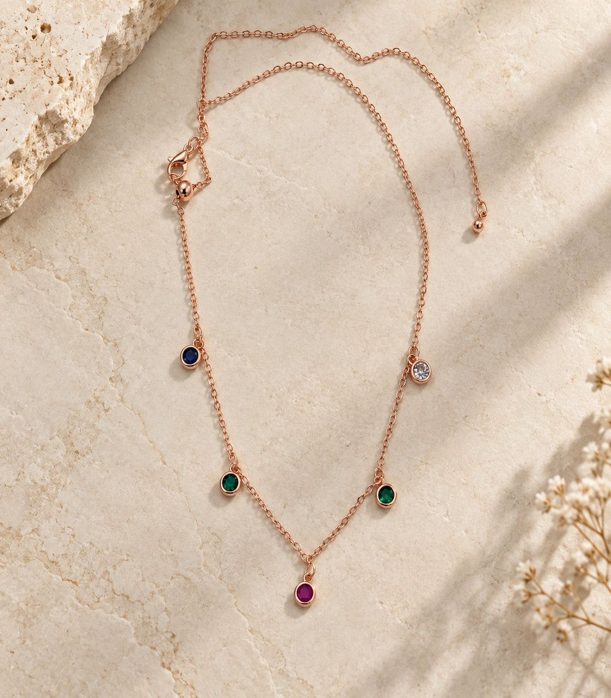JIMIKI Rose Gold Multicolor Five-Stone Station Necklace, five-stone necklace arranged on a pale textured surface #color_multicolour