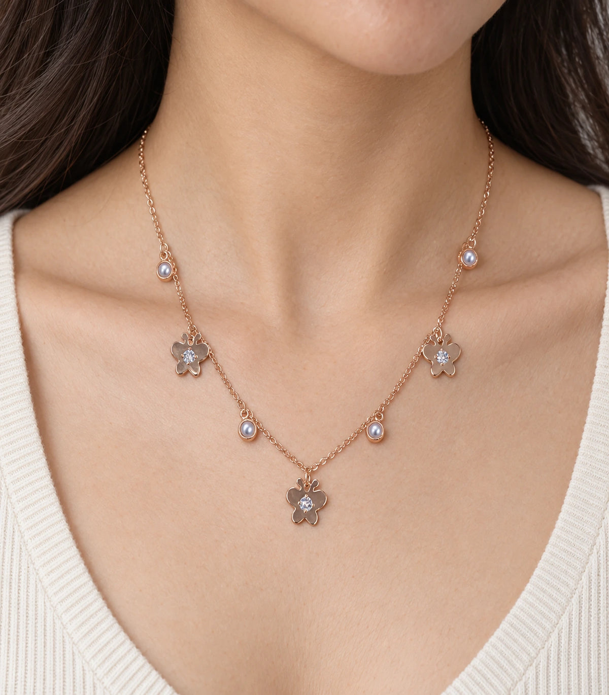 JIMIKI Rose Gold Pearl Effect Butterfly Charm Necklace - worn closeup of butterfly charms and pearl-effect drops #color_rose-gold